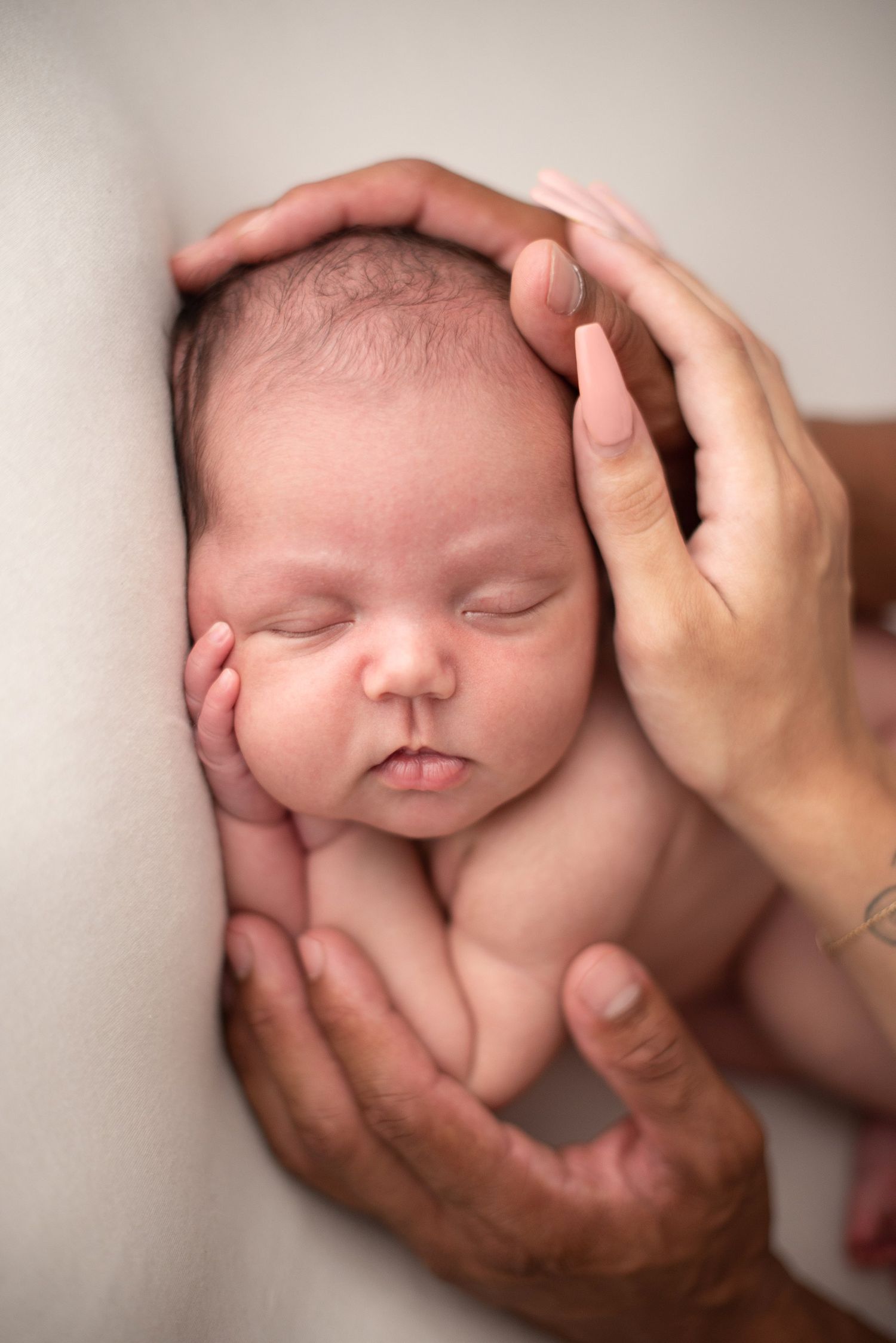 Close-up portrait of sleeping newborn baby's face cradled in gentle hands.