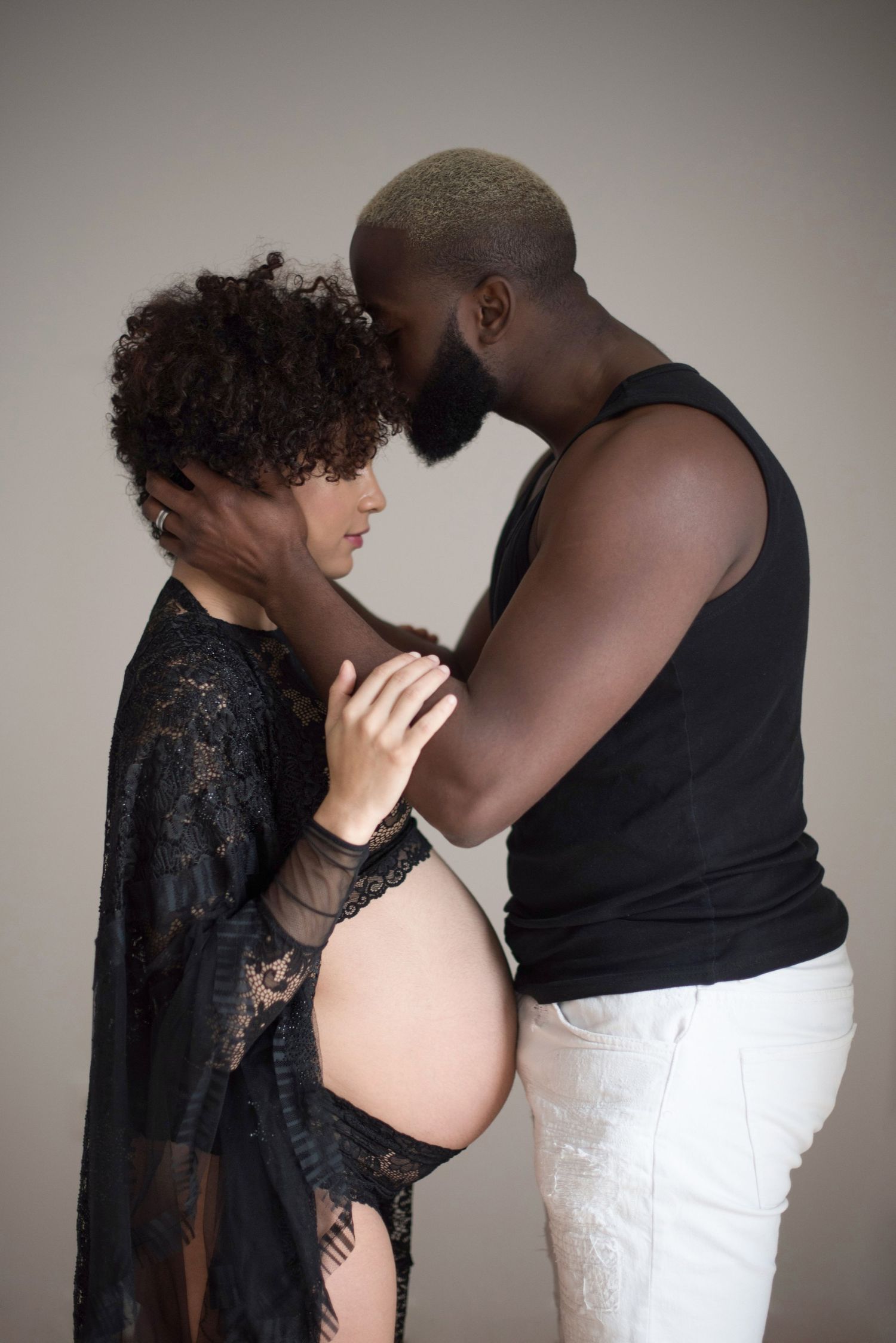 Intimate maternity photo of couple in black clothing against grey background.