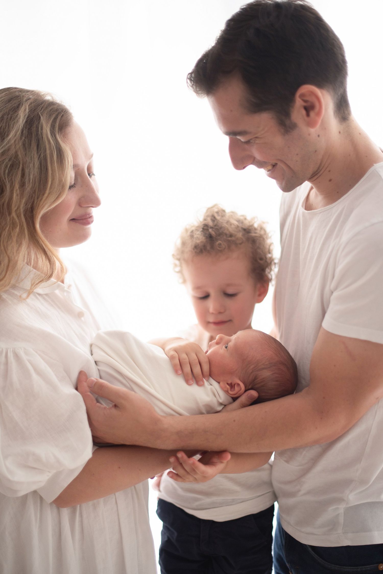 Intimate family moment with newborn baby in soft white studio setting.