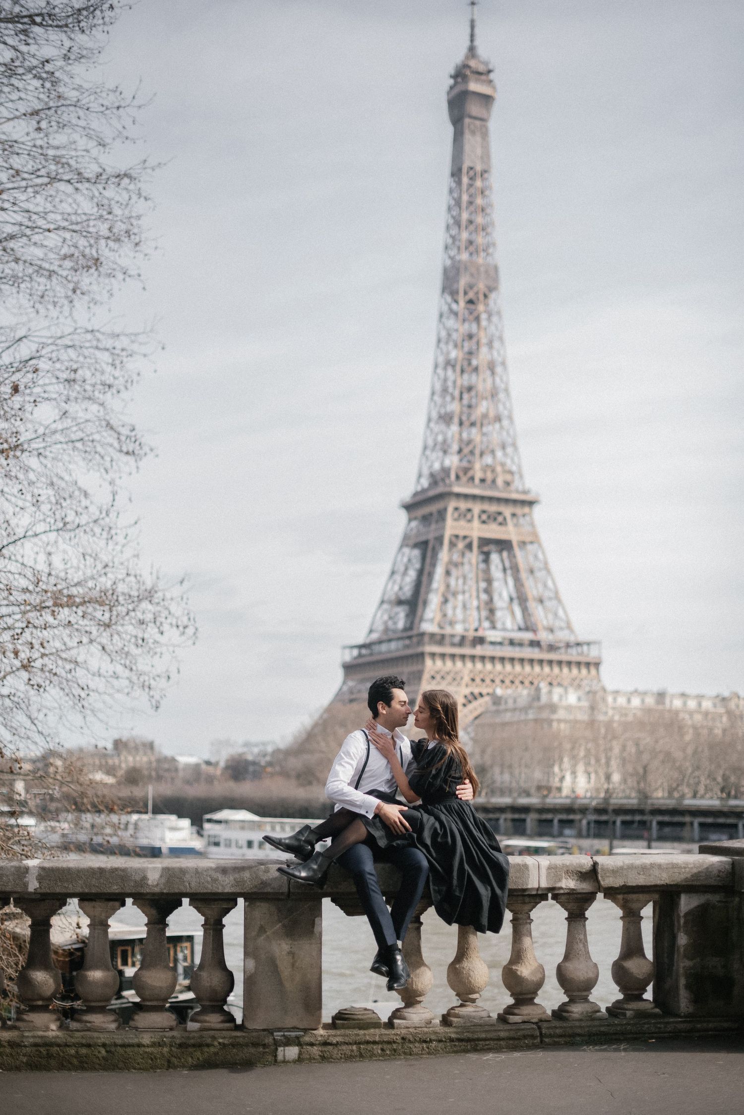 Romantic couple sitting on stone balustrade with Eiffel Tower in background.