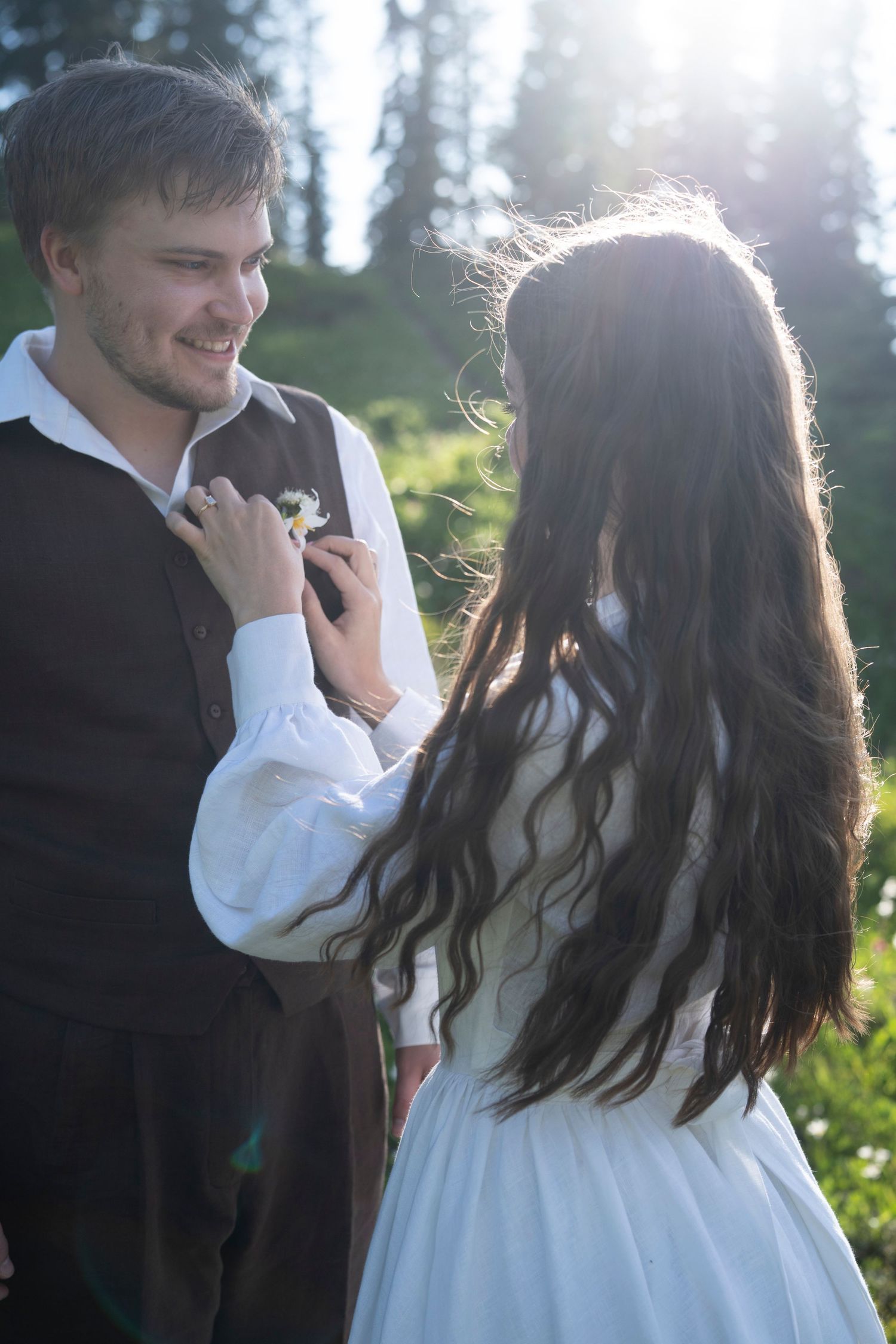 A romantic couple in formal attire share an intimate moment in a sunlit forest setting.