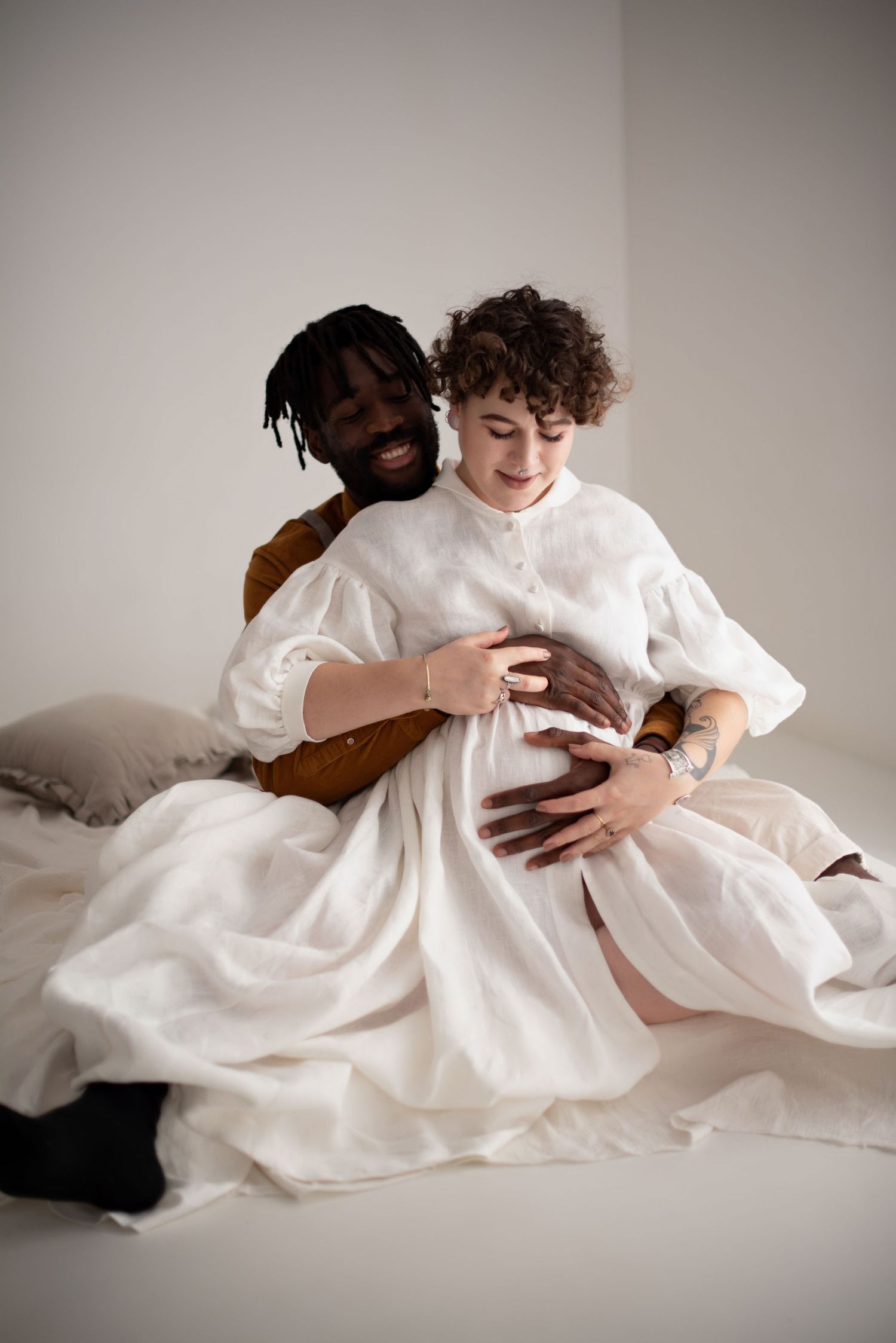 An intimate maternity portrait with couple embracing on white bedding.