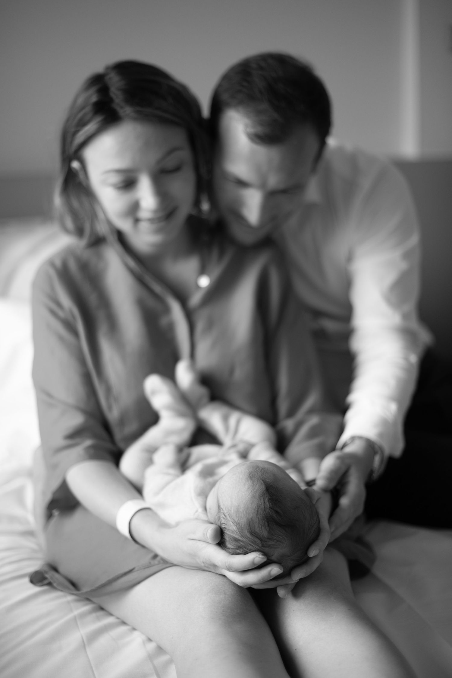 A tender black and white portrait of parents cradling their newborn baby in an intimate family moment.