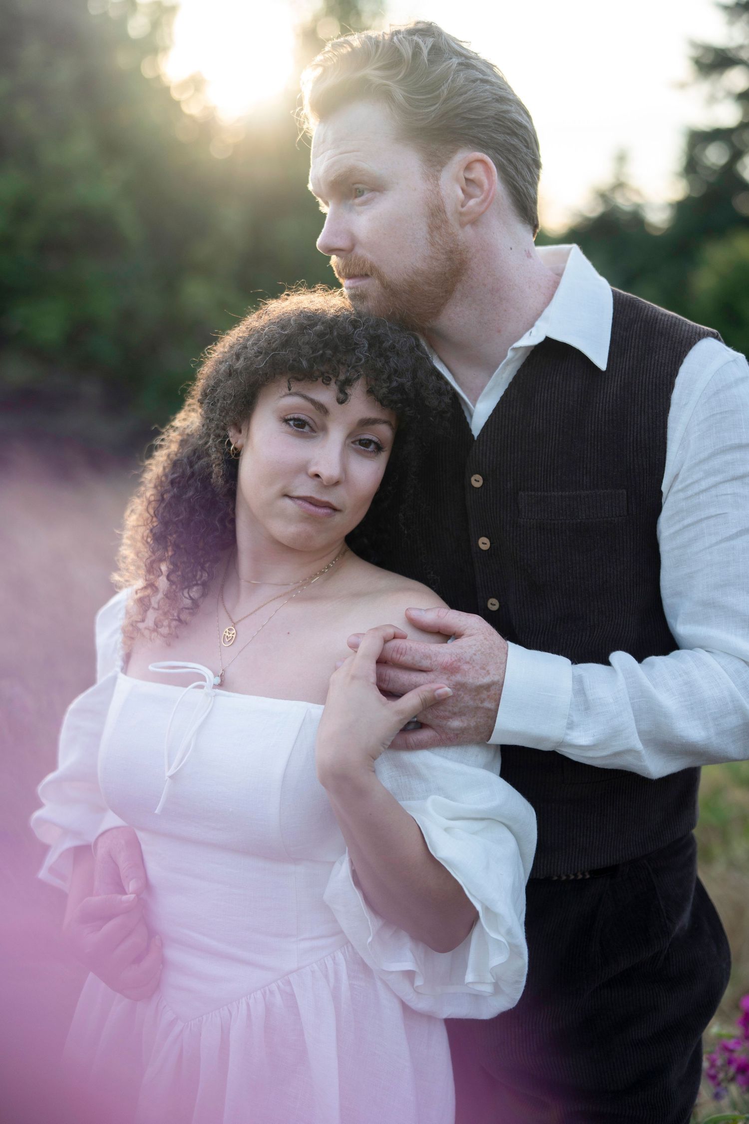 A romantic couple embraces outdoors during sunset in a soft pink ethereal scene with vintage styling.