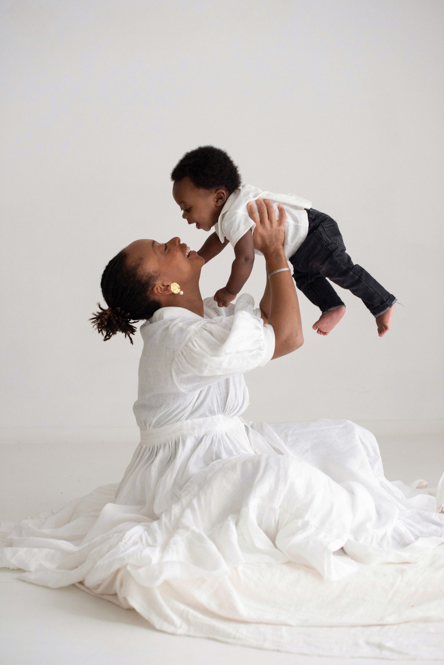 A tender moment captured as a figure in white lifts a small child playfully against a light background.