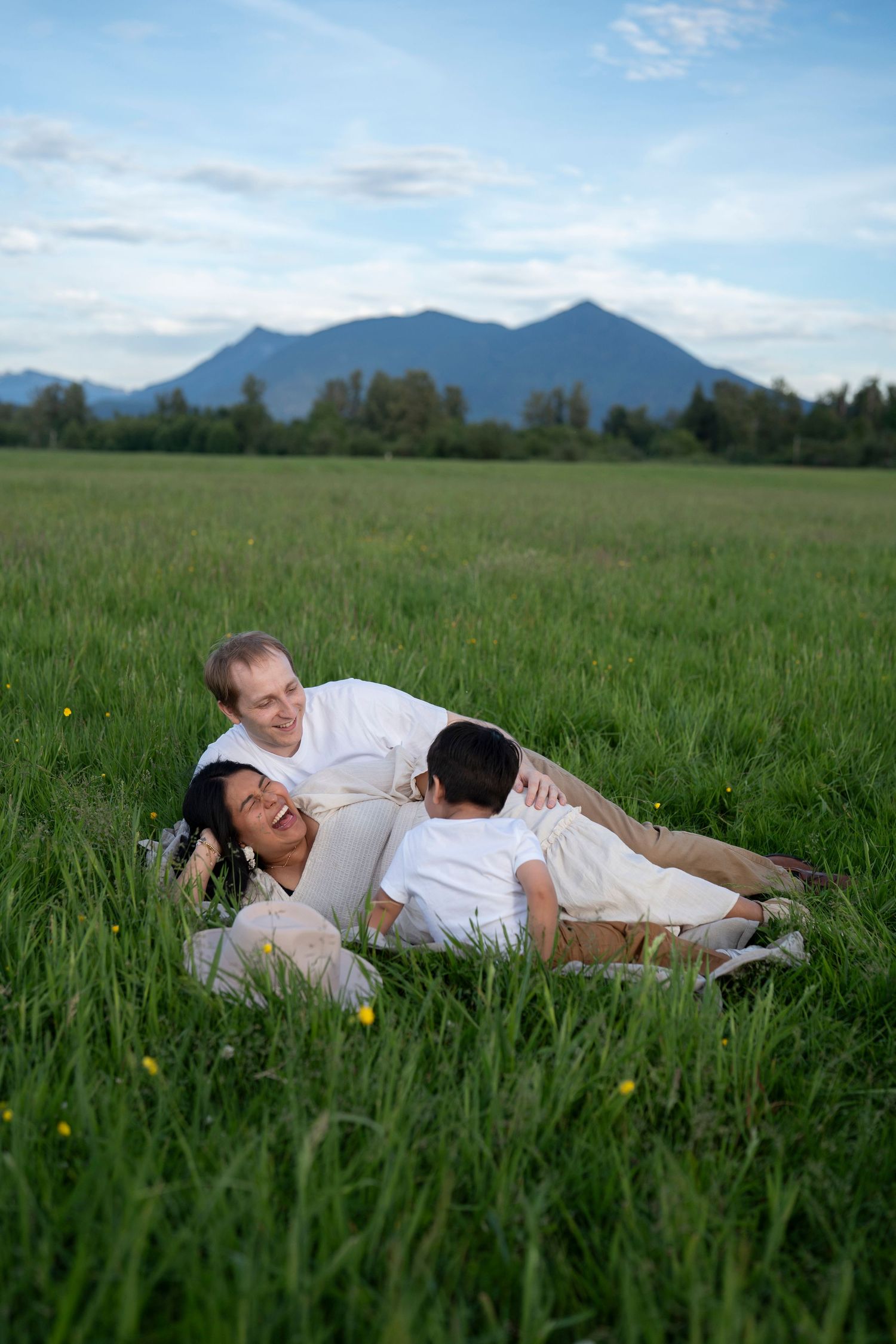 A couple laying together in a lush green meadow field with mountains visible in the distant background.