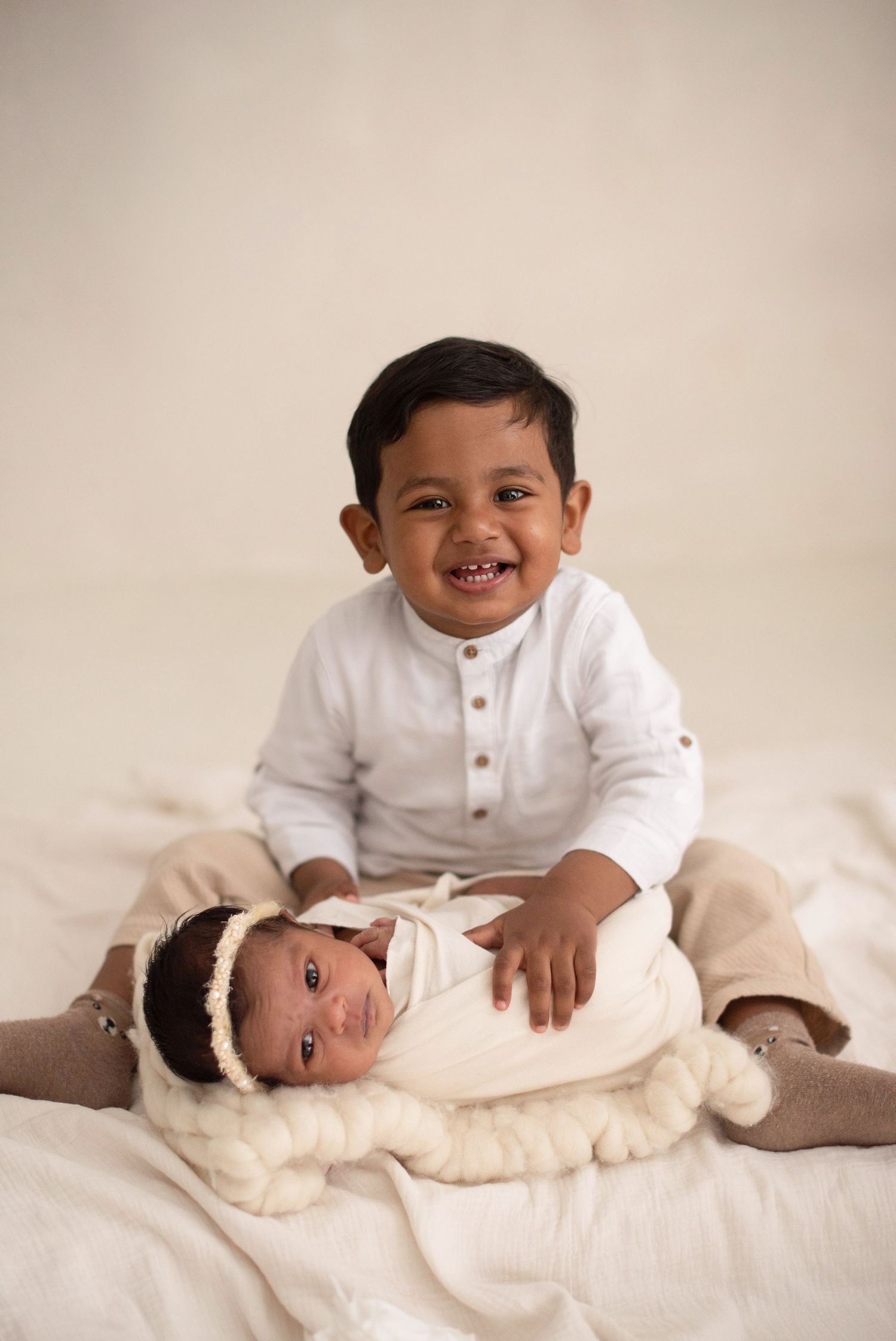 Two siblings share a tender moment on white bedding during a studio photoshoot.