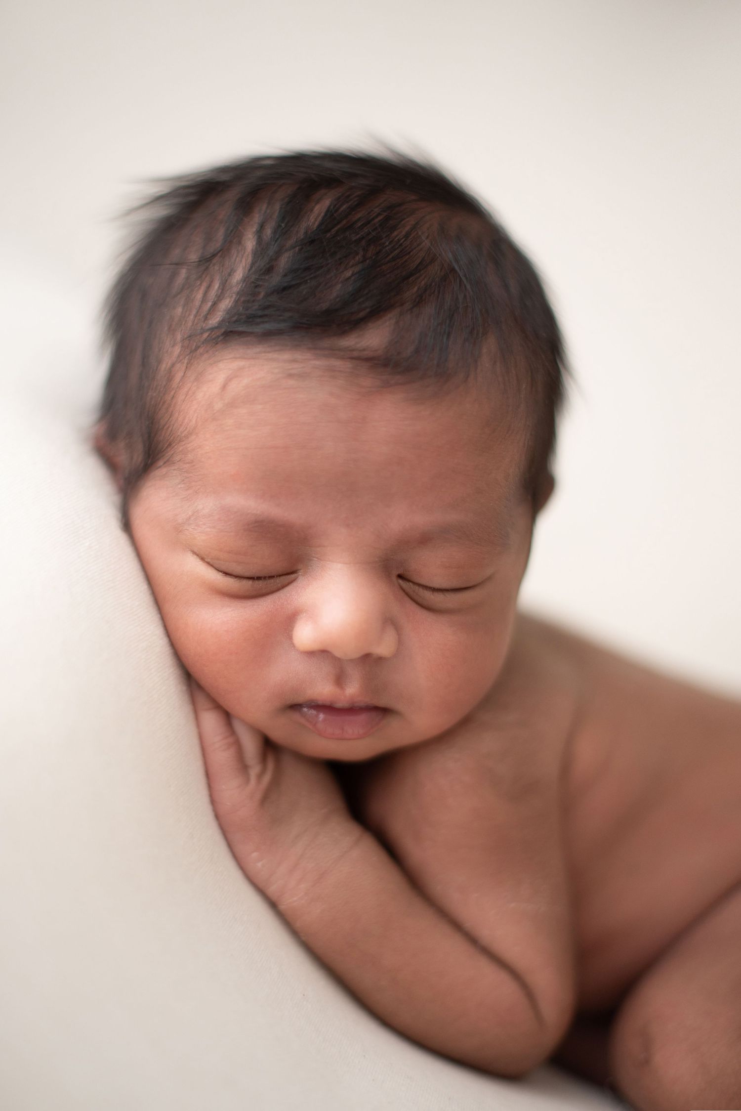 A peaceful sleeping newborn baby rests against a light backdrop in a gentle pose.