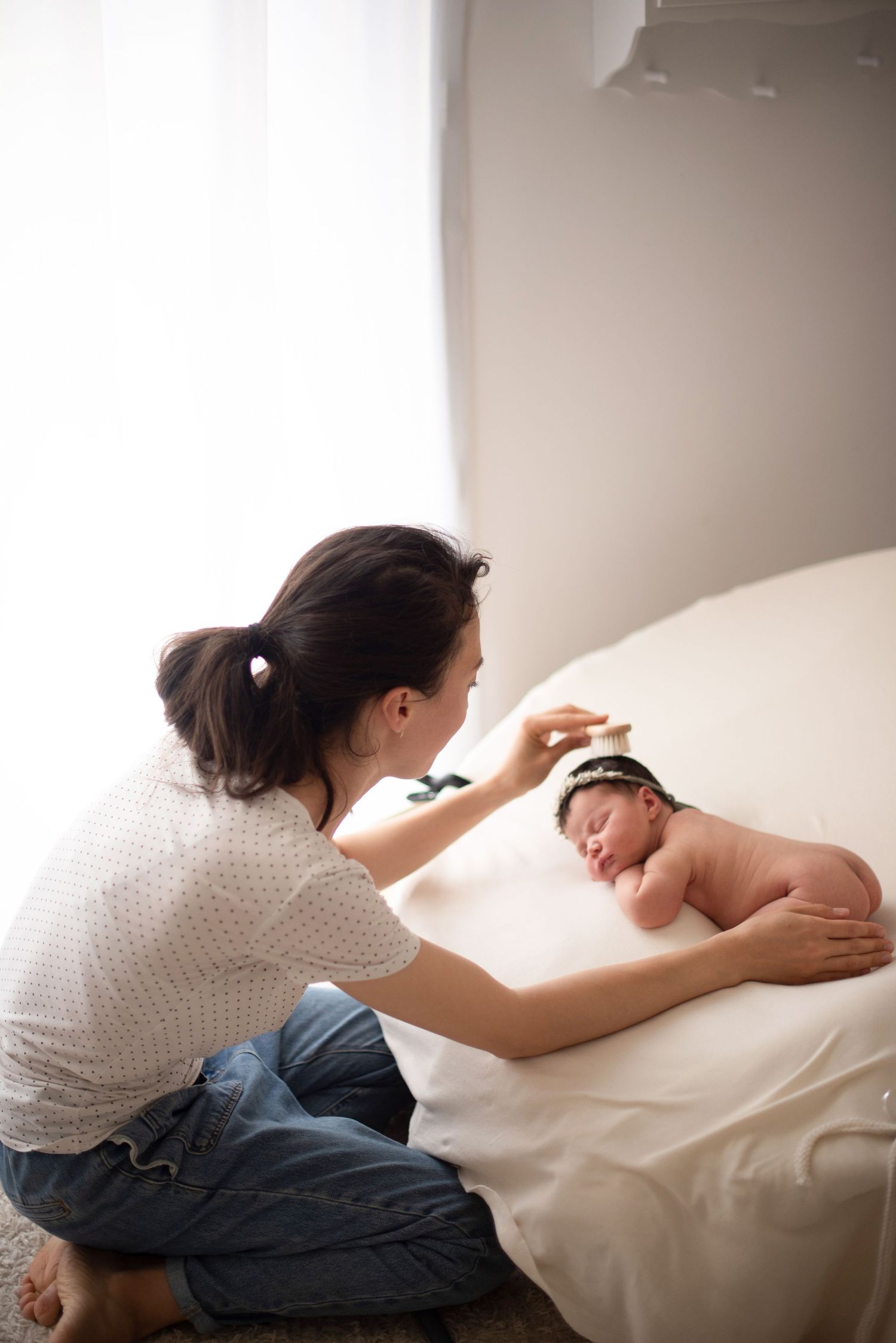 Gentle newborn photography session with baby sleeping on white blanket as photographer delicately brushed their hair.