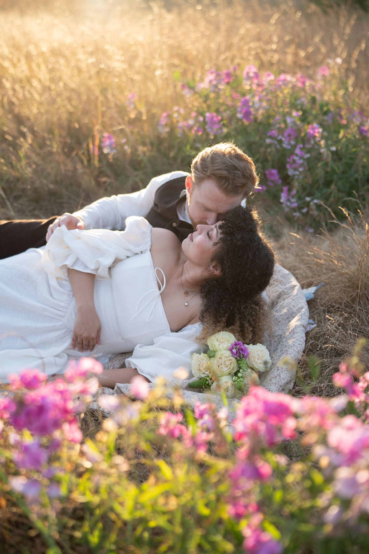 Couple sharing an intimate moment among colorful wildflowers in a sun-drenched meadow at golden hour.