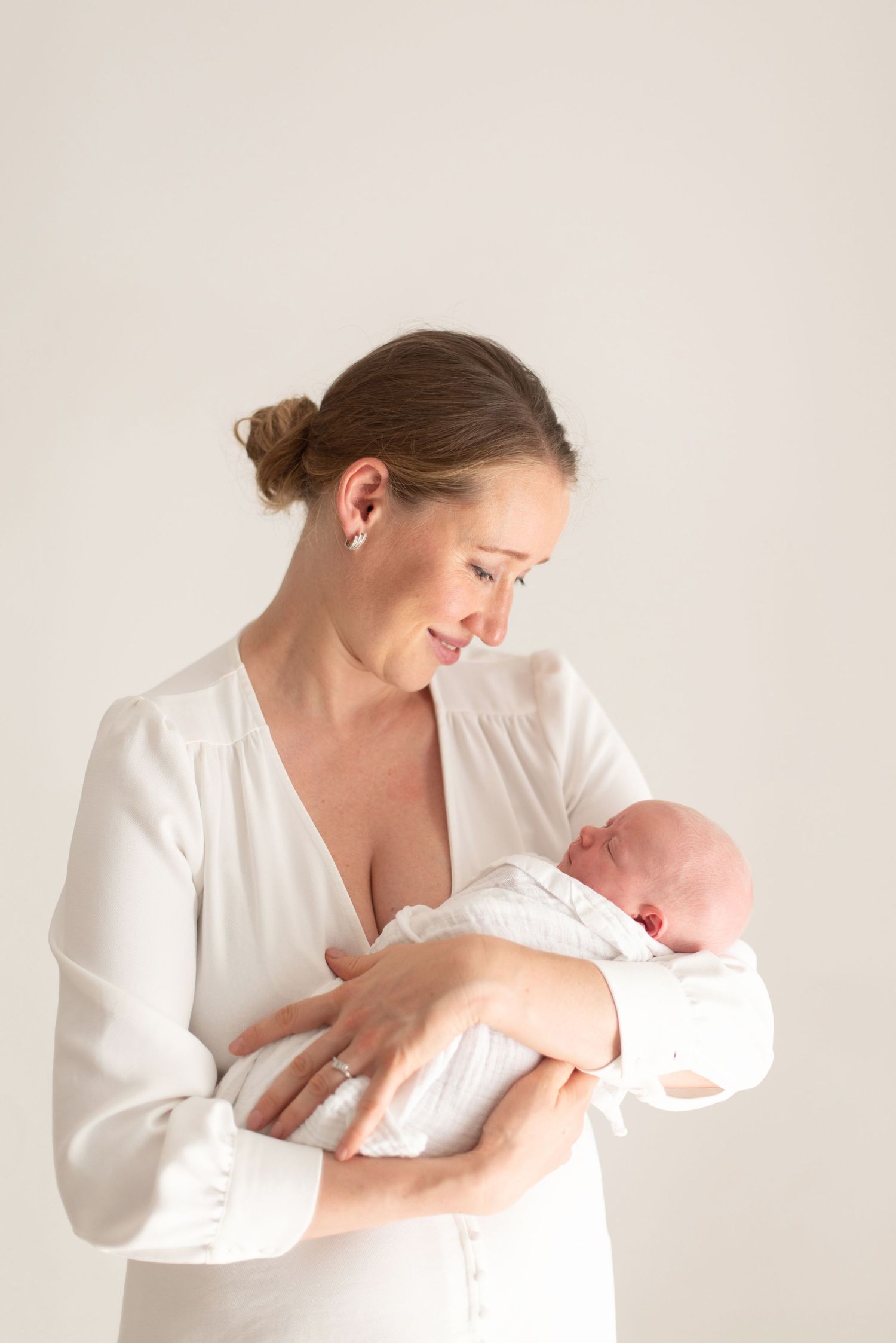 An intimate portrait of a maternal moment with a newborn baby in white clothing.