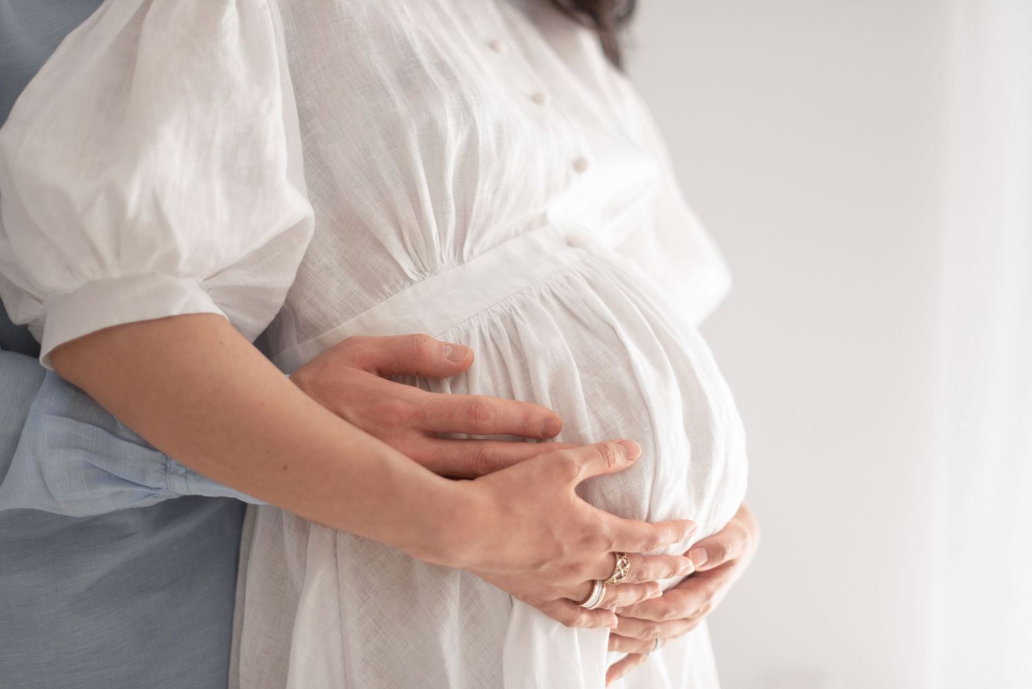 Close-up of hands cradling pregnant belly in flowing white maternity dress.