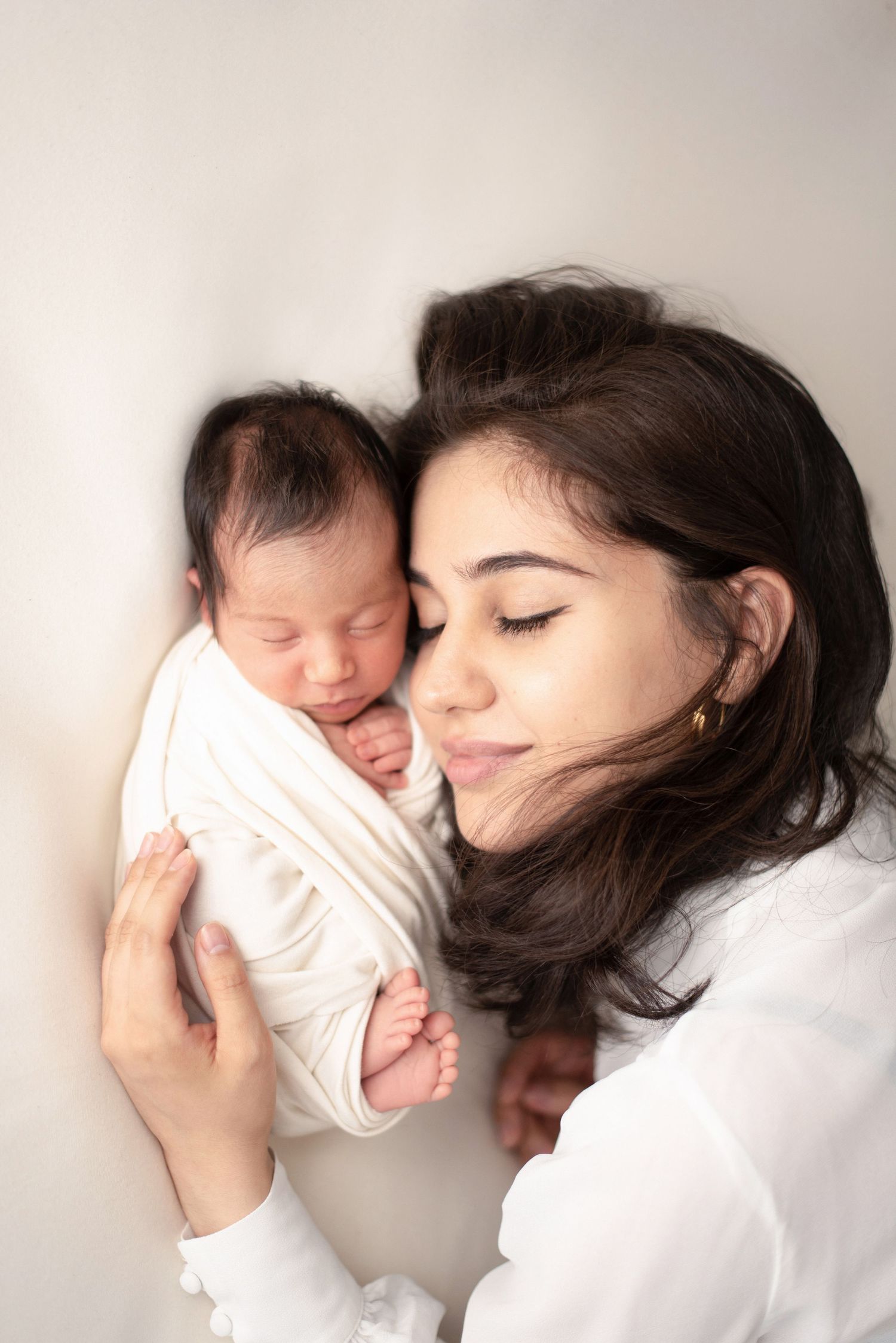 A tender moment between a parent and newborn baby wrapped in white against a light background.