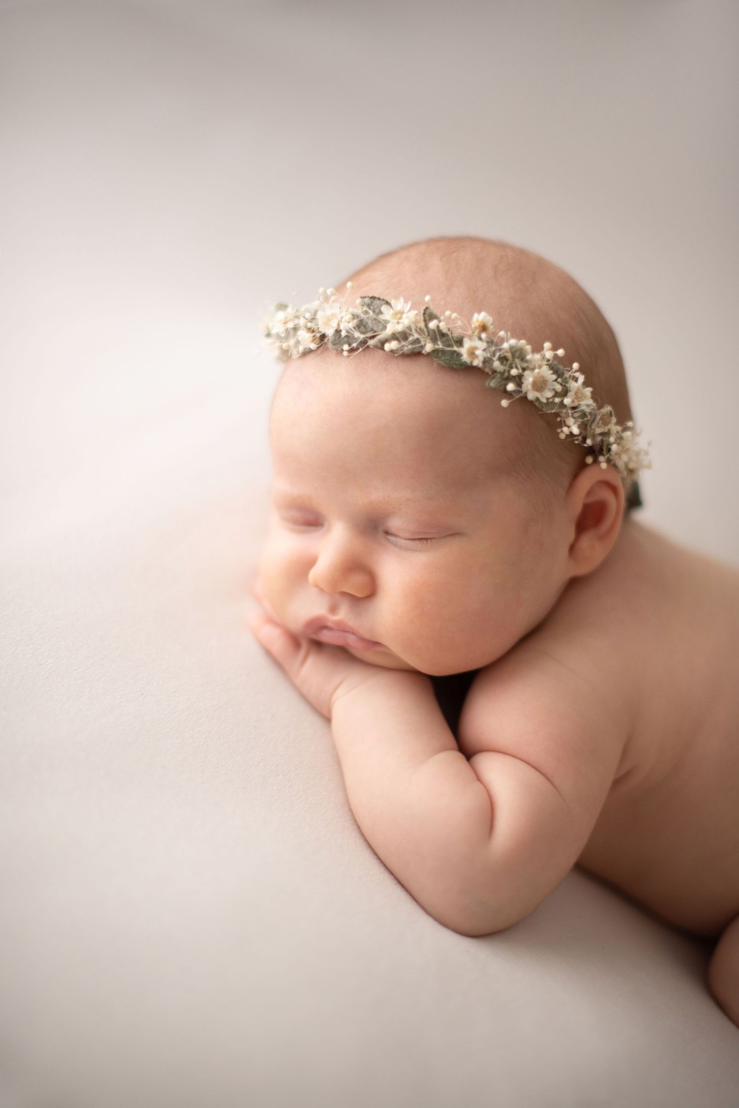 Sleeping baby wearing white floral crown during professional newborn photography session.