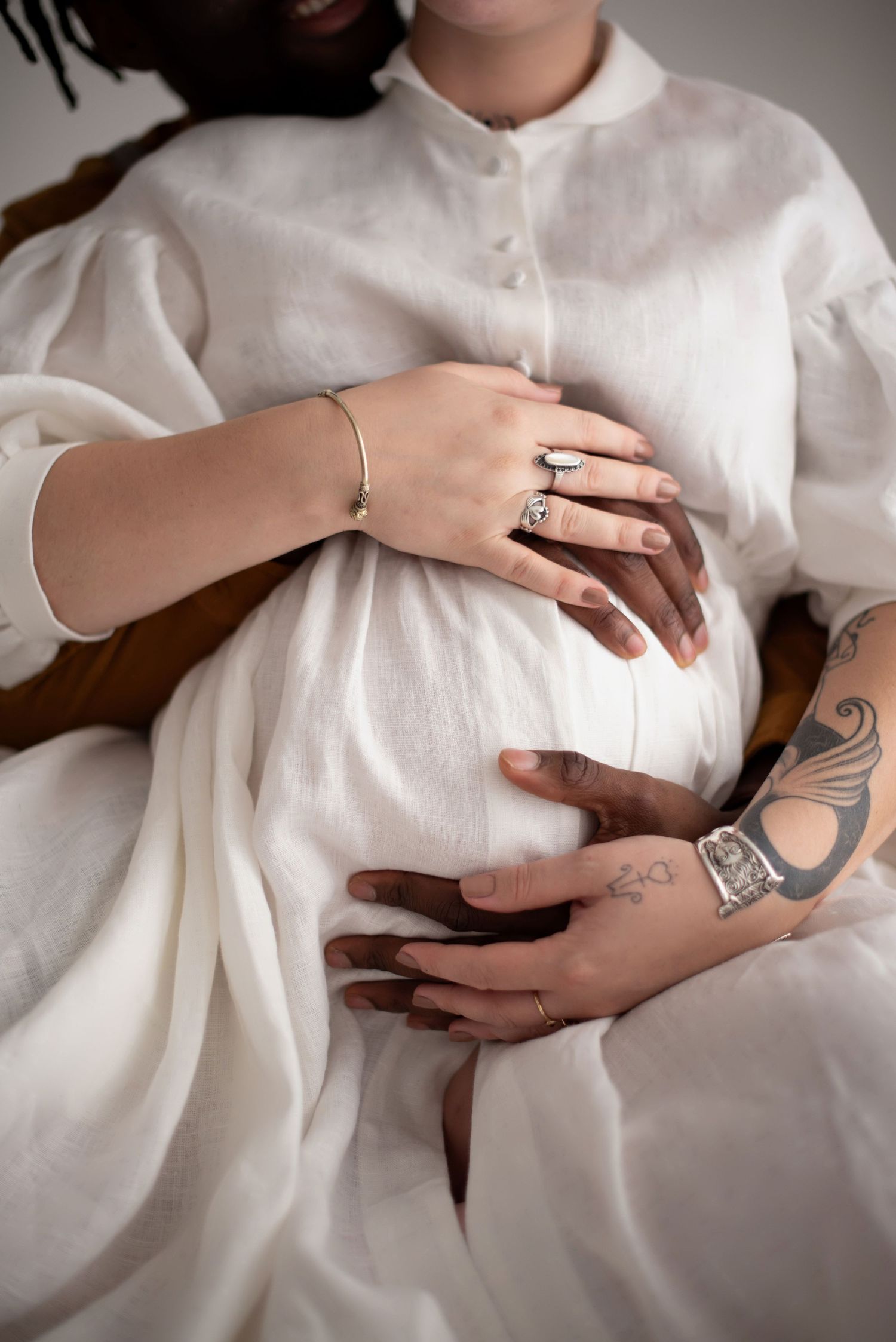 Hands rest gently on a white linen maternity dress, showing baby bump of a pregnant woman in Seattle