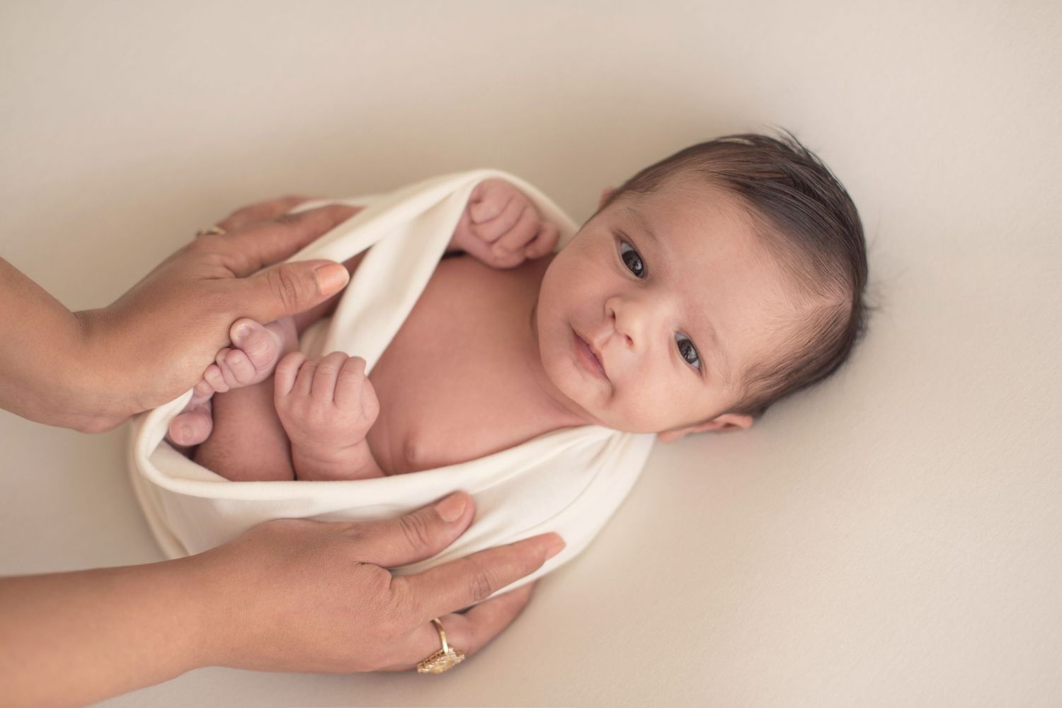 Gentle hands supporting a swaddled infant against white background.