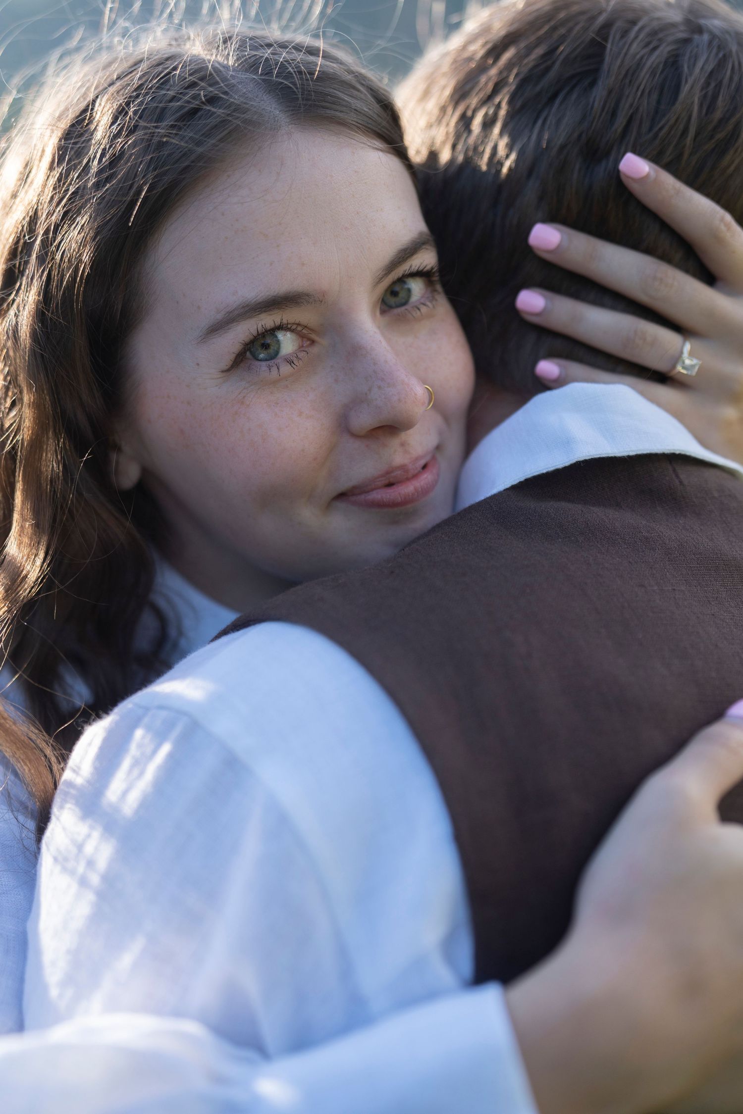 A couple embraces in a tender moment outdoors with sunlight filtering through the trees.