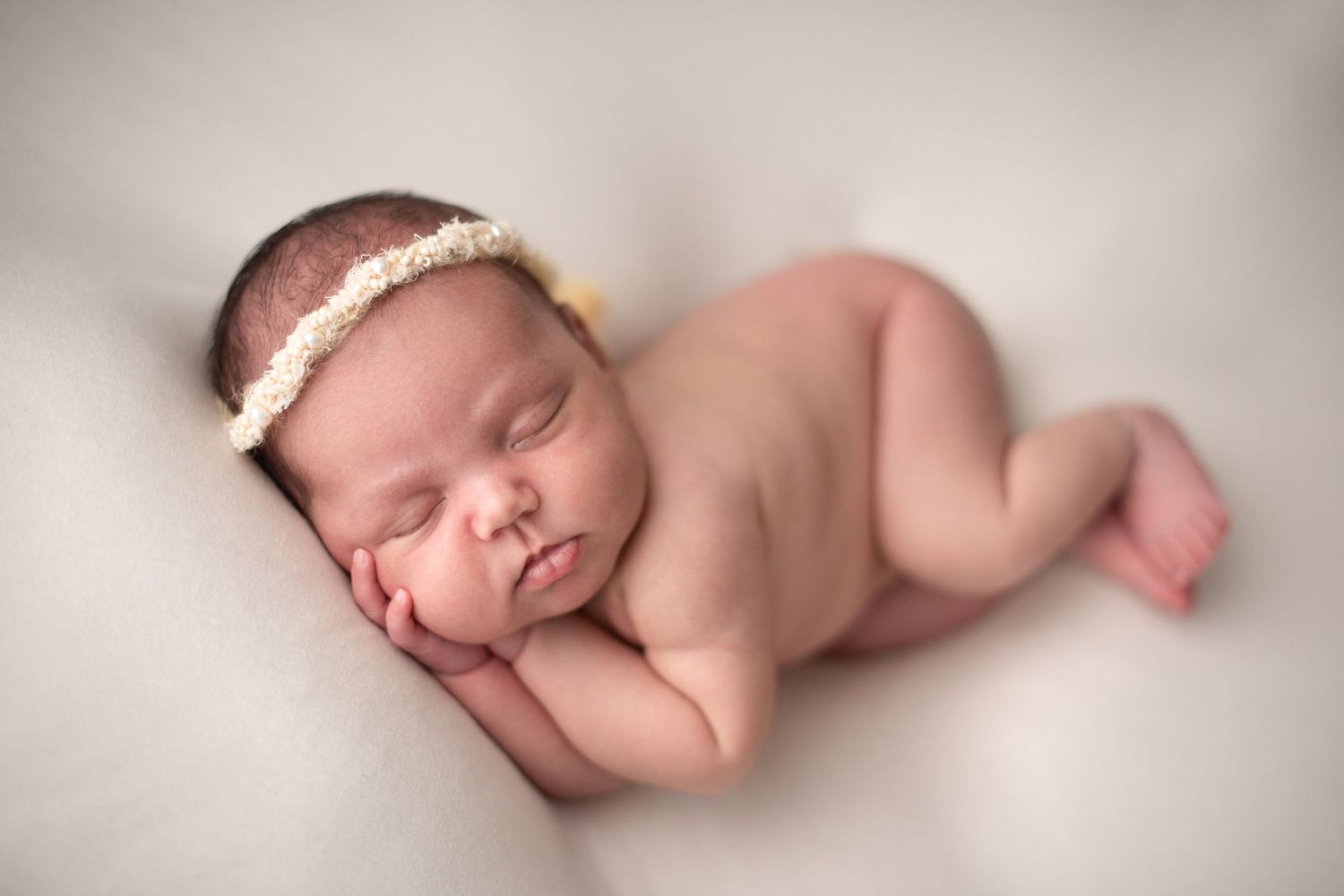 Sleeping newborn baby wearing pearl headband in gentle resting pose.