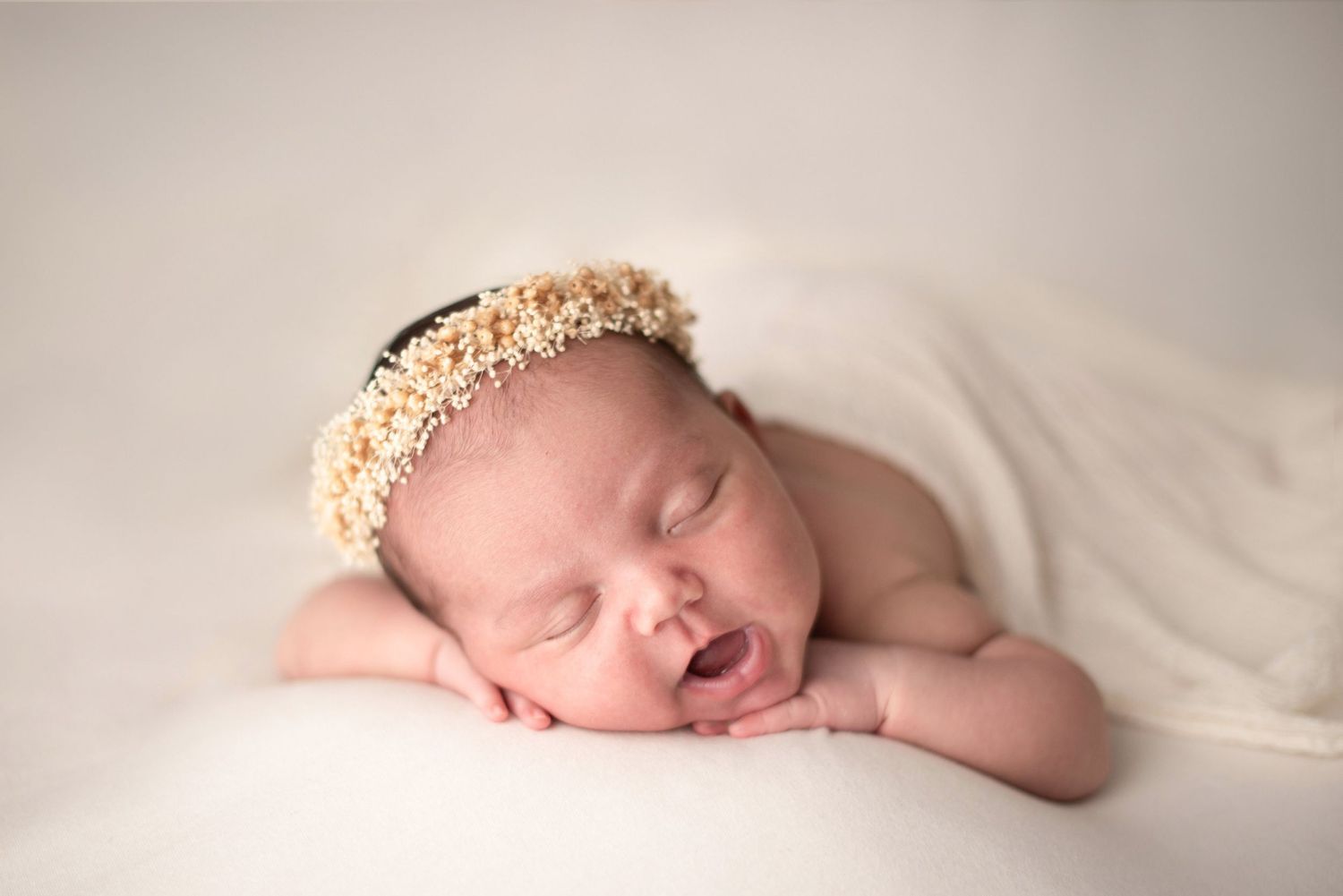 Peaceful newborn with gold crown accessory sleeping on white fabric.