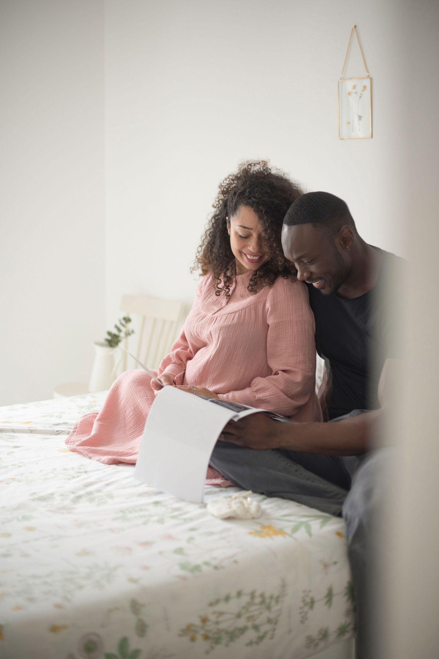 Expecting couple shares a joyful moment while sitting together on a floral patterned bed.