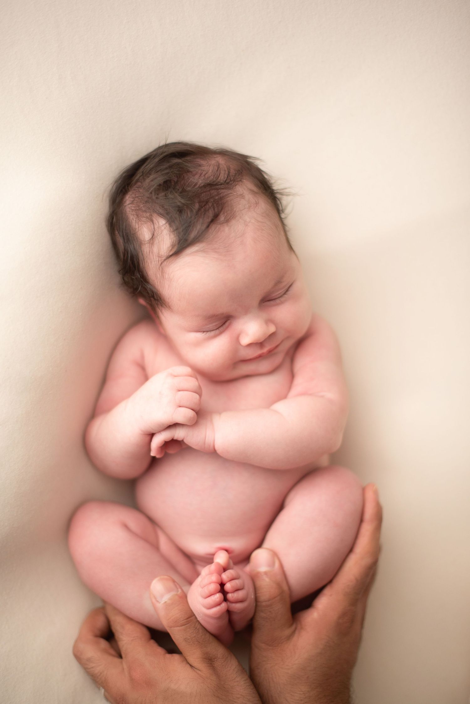 Peaceful newborn baby cradled in gentle hands against a light backdrop.