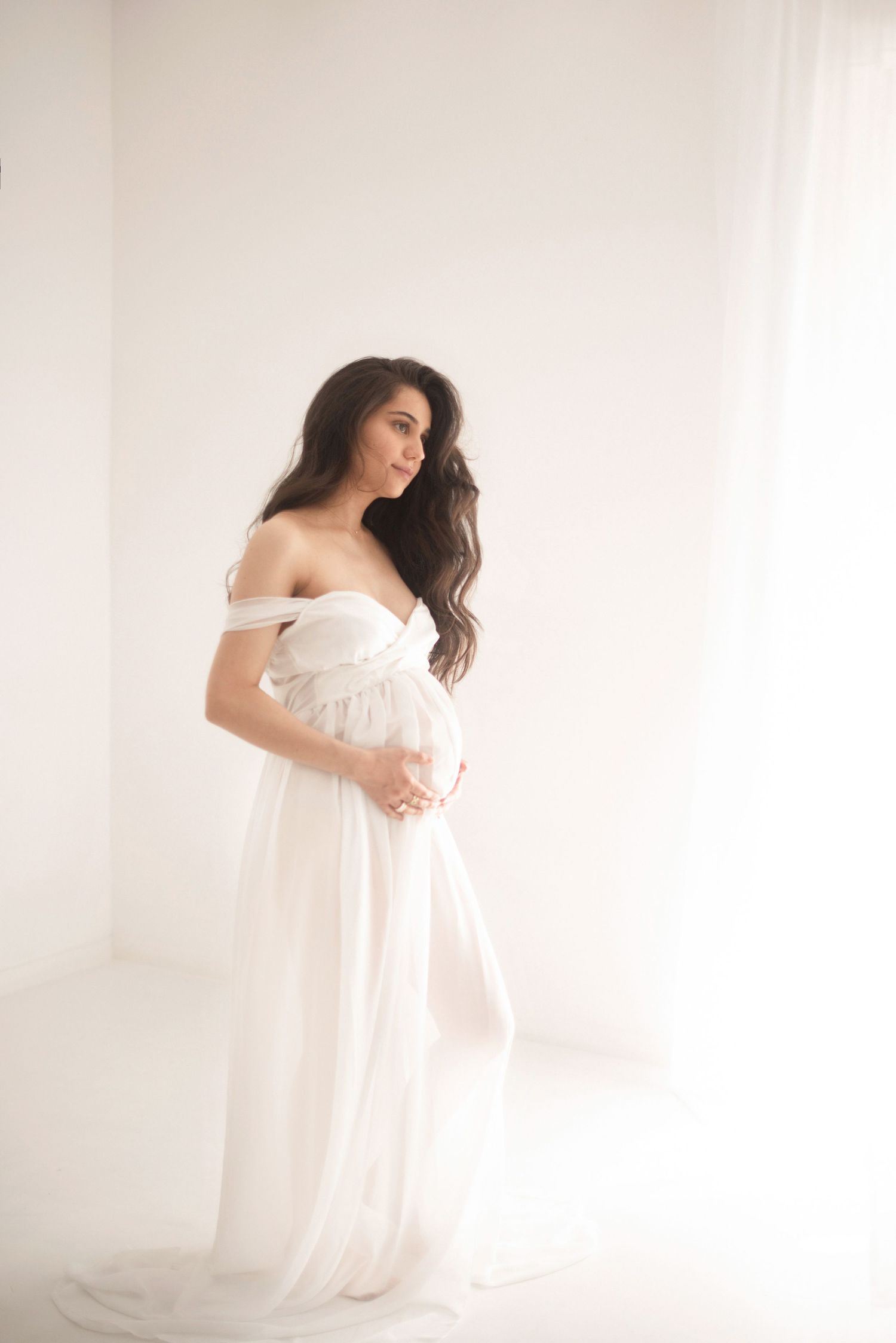 Soft, dreamy maternity photo with woman in off-shoulder white gown.