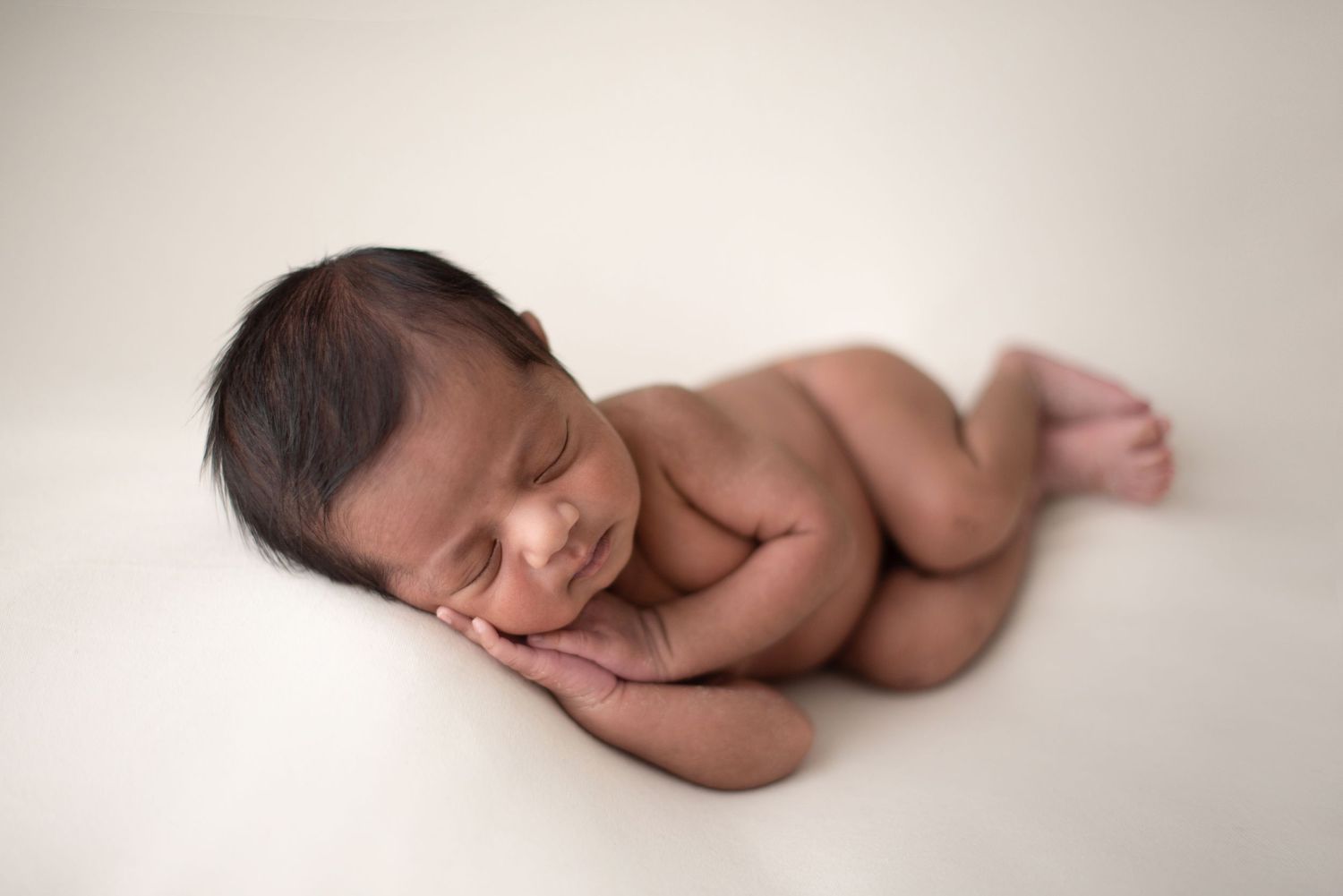 A sleeping newborn baby lies peacefully on their side against a white background.