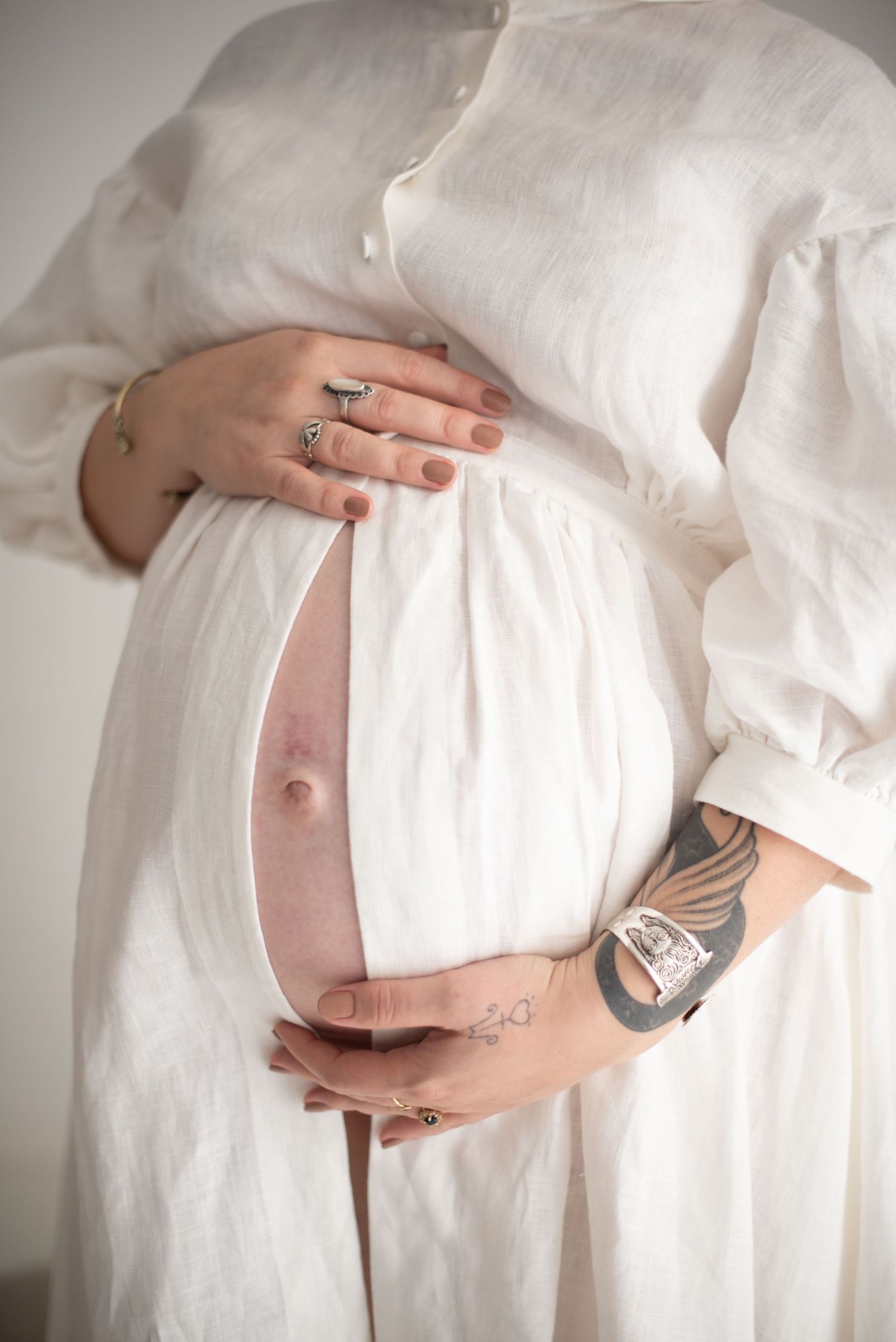 Close-up photo of hands tenderly touching a pregnant belly with visible tattoos.