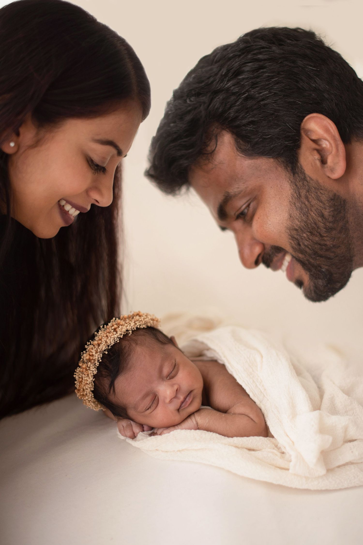 A sleeping newborn wearing a golden crown is surrounded by loving gazes in a tender family portrait.