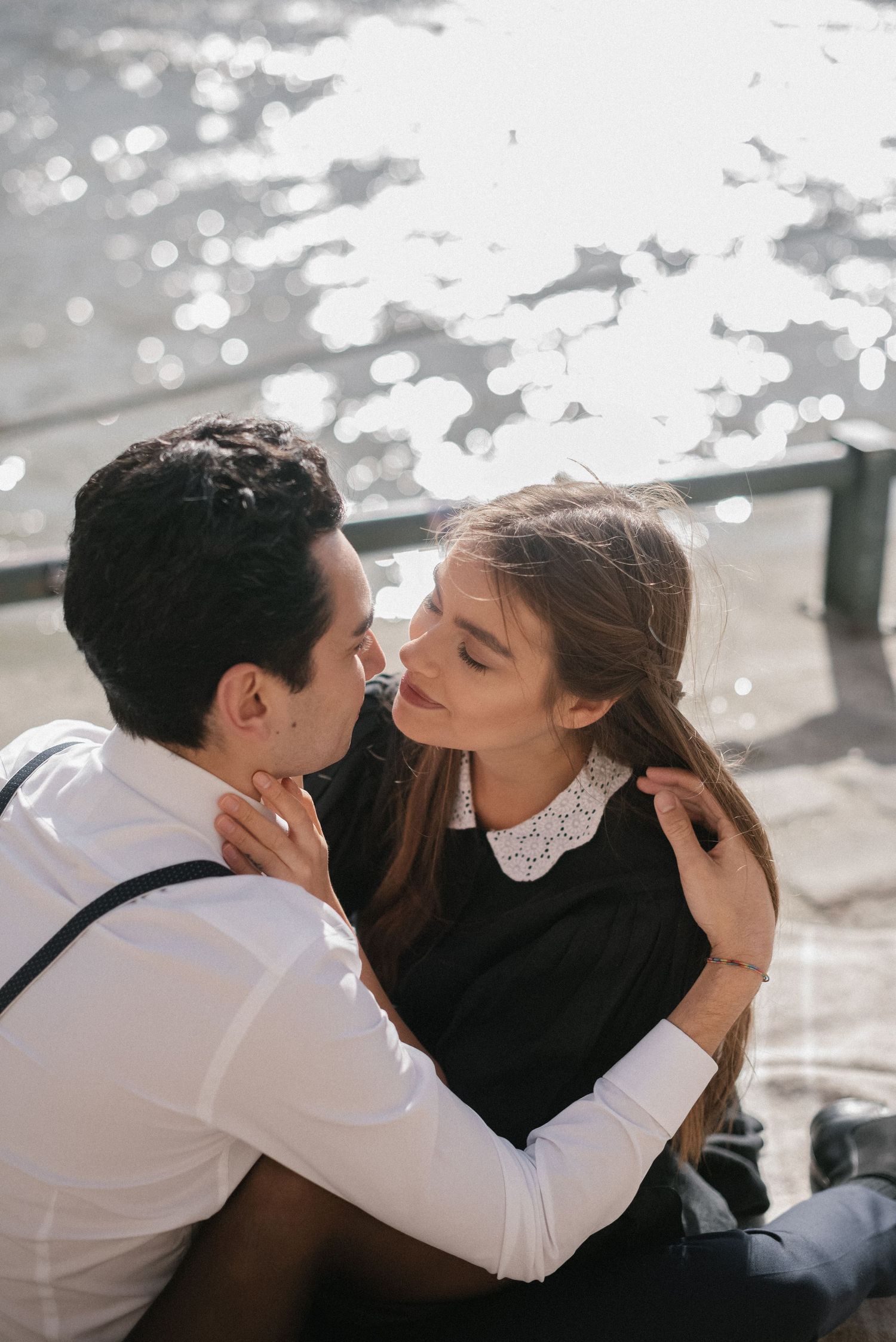 Couple in classic attire sharing intimate moment by river.