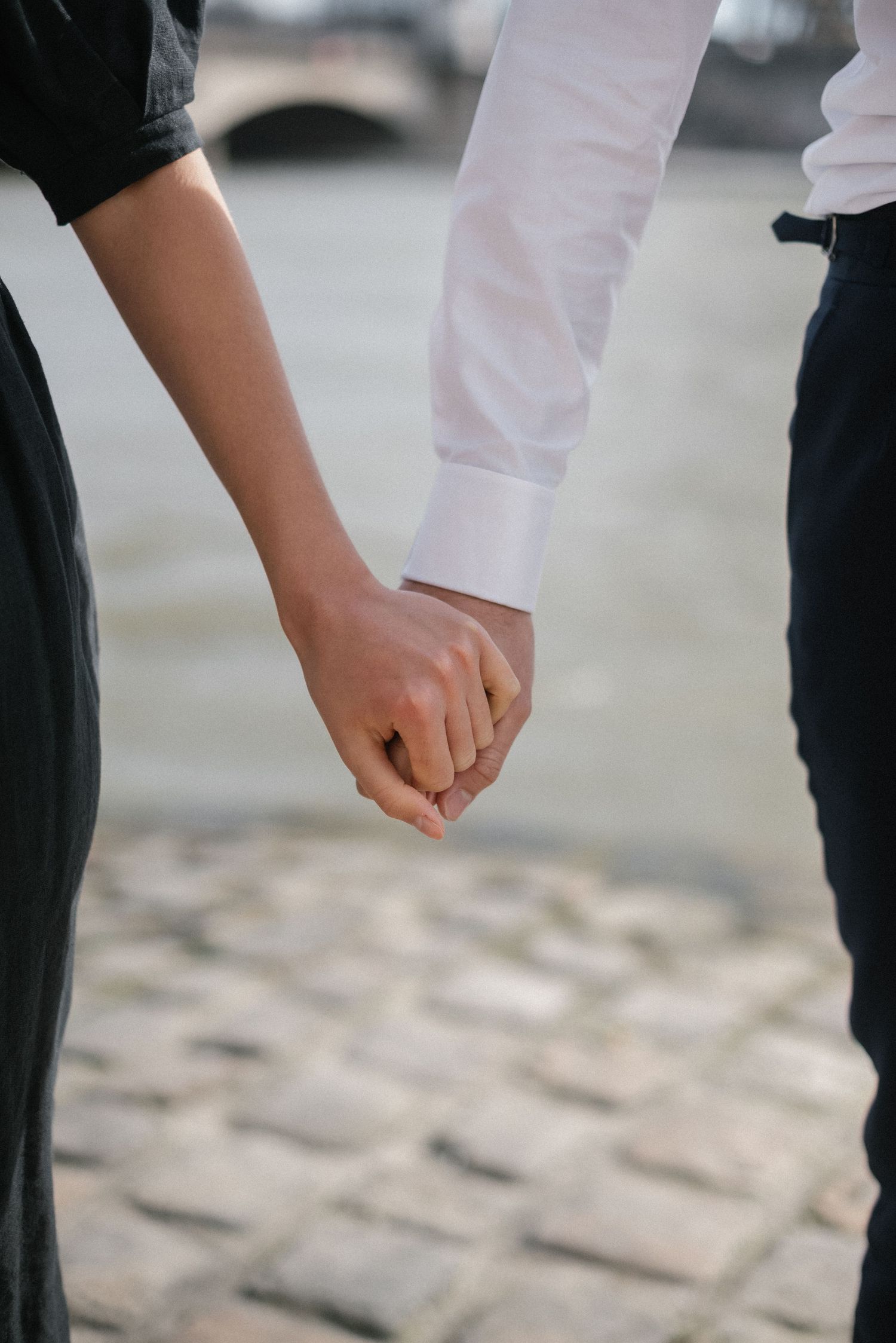 Two people holding hands tenderly on cobblestone streets of Paris.