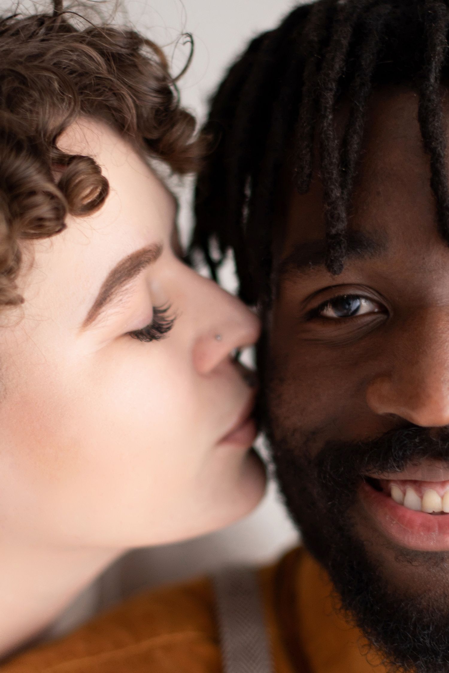 An intimate close-up photo of an interracial couple showing affection against a white background.