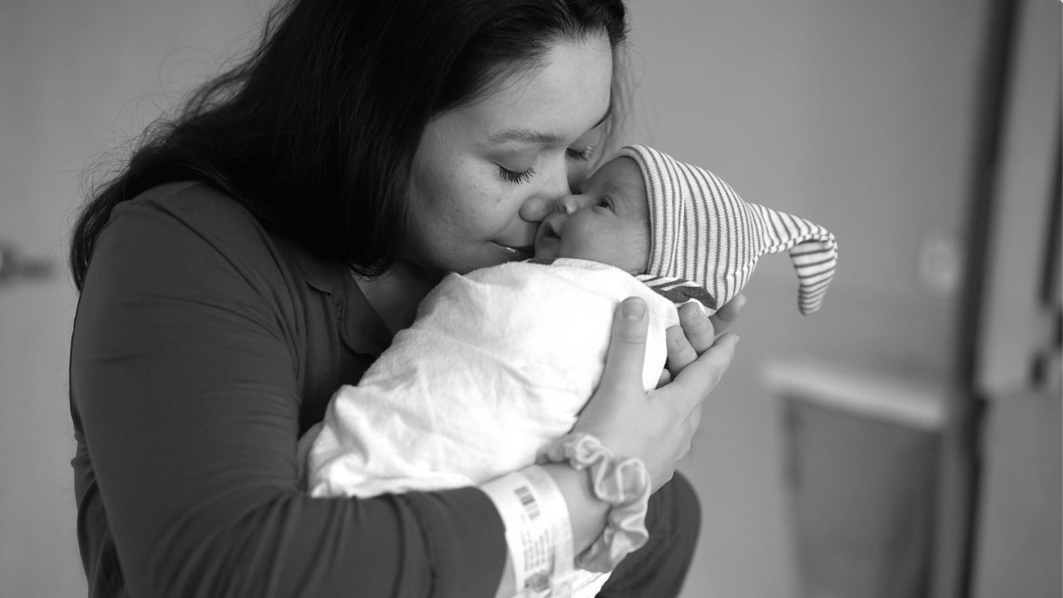 A tender moment captured in black and white as a mother lovingly embraces her sleeping newborn baby.
