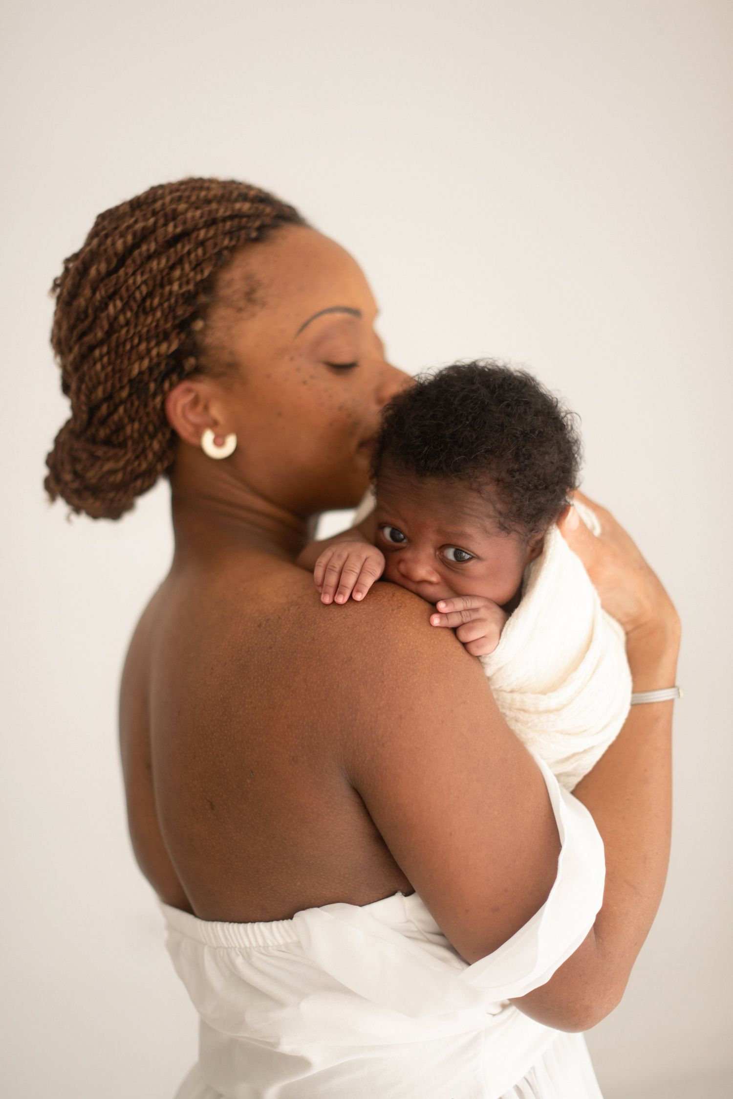 Intimate portrait of mother embracing baby against white background.