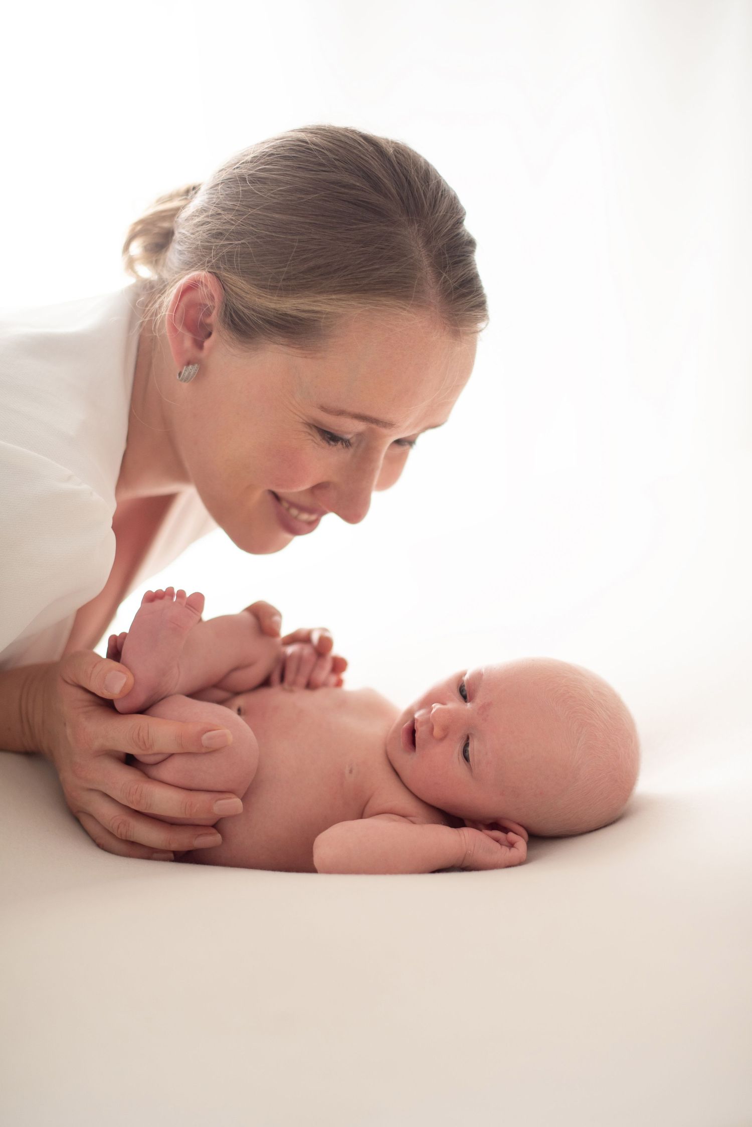 Tender moment between parent and newborn baby lying on white backdrop in soft natural lighting.