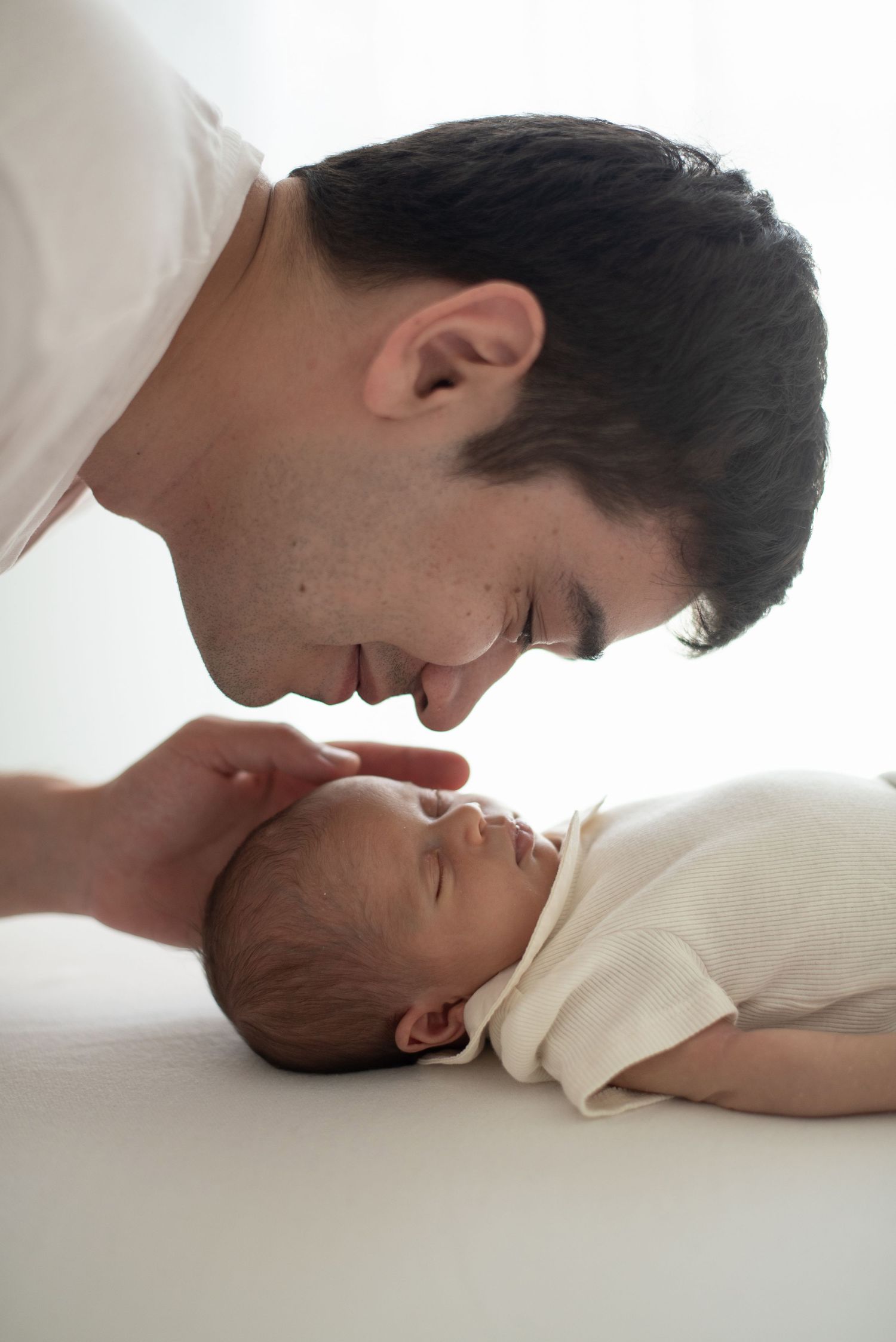 Tender moment between parent and newborn baby on white bedding.