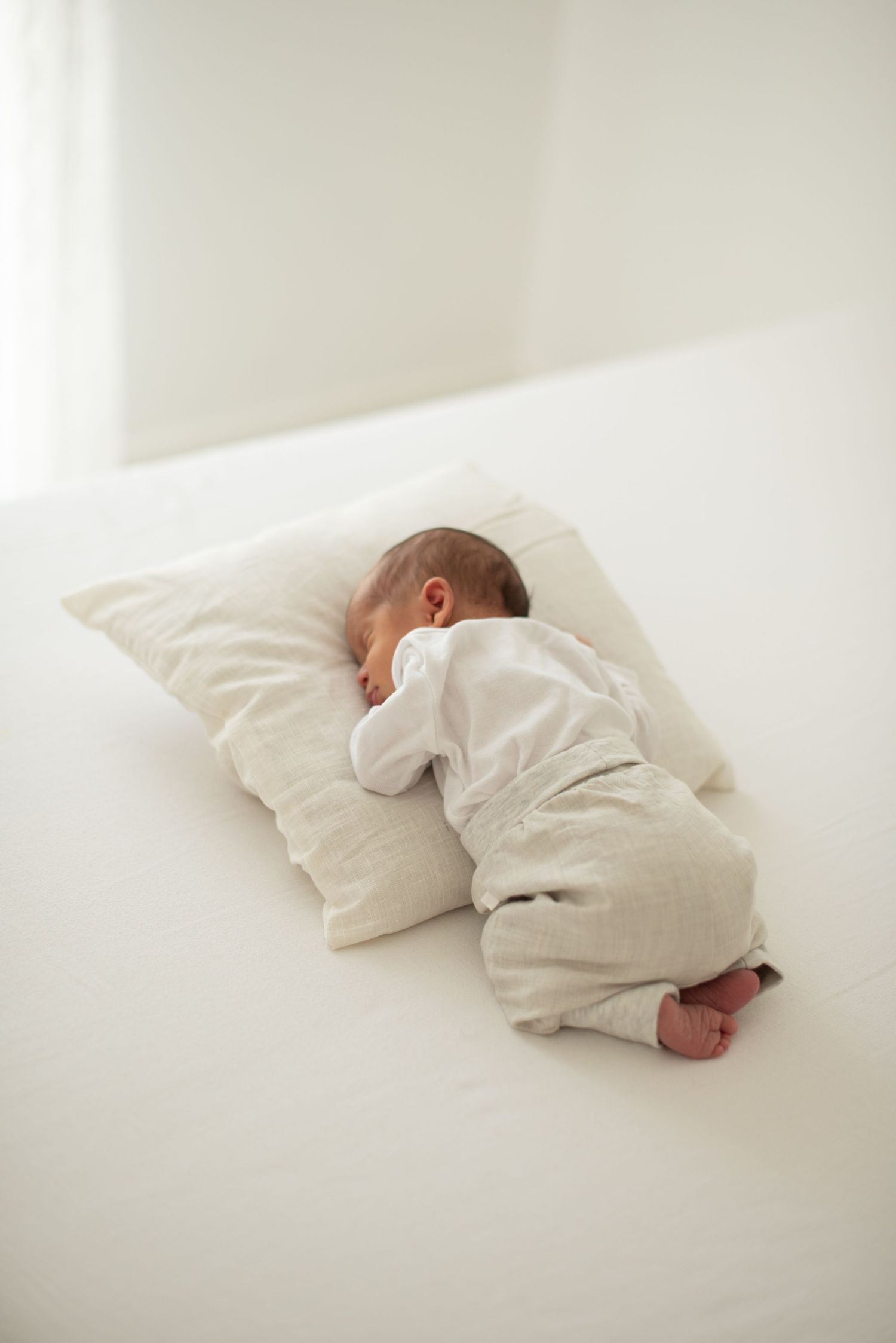 Sleeping newborn baby in white onesie resting on soft white pillow.