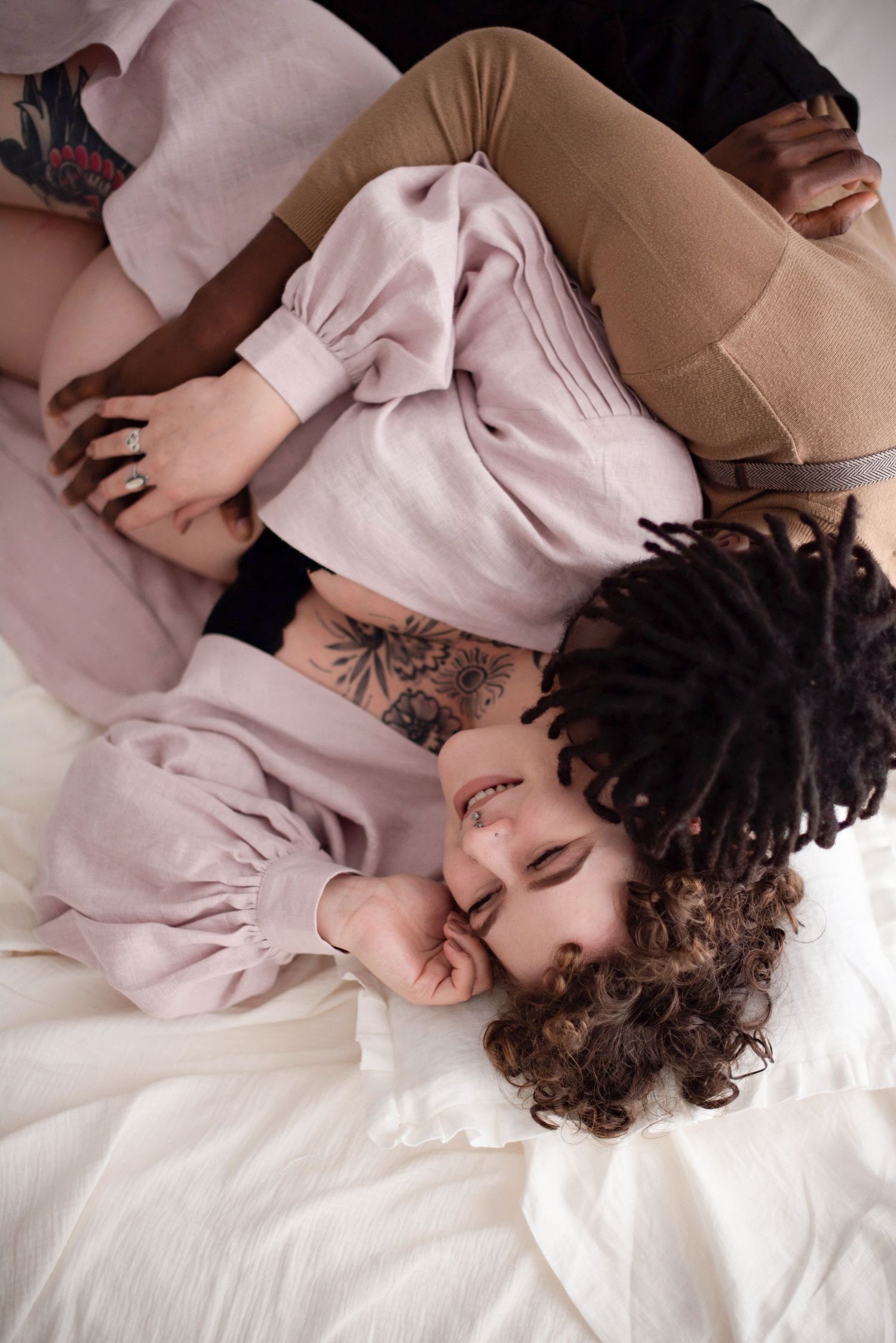 Top view of couple in romantic pose on white bedding during maternity photoshoot.