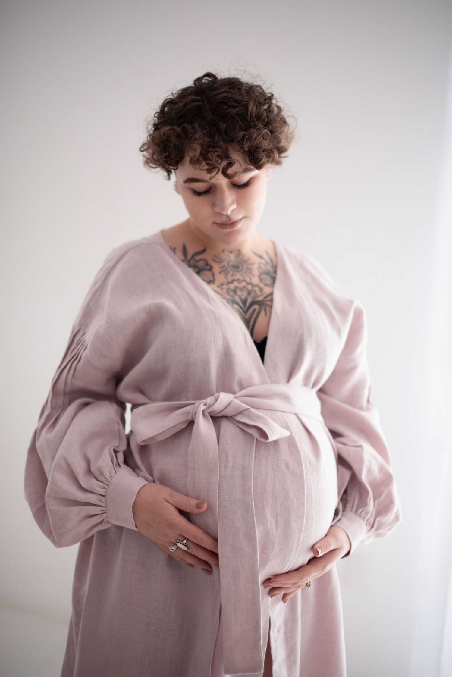 Expectant parent in pink dress with tattoos gently holds baby bump.
