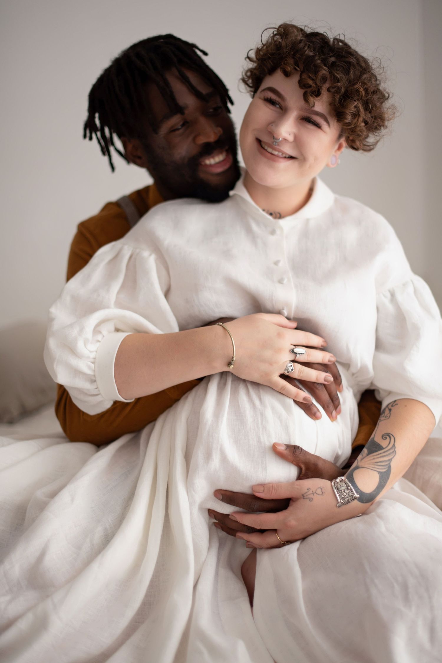 A joyful maternity photo showing a couple's embrace against neutral backdrop.