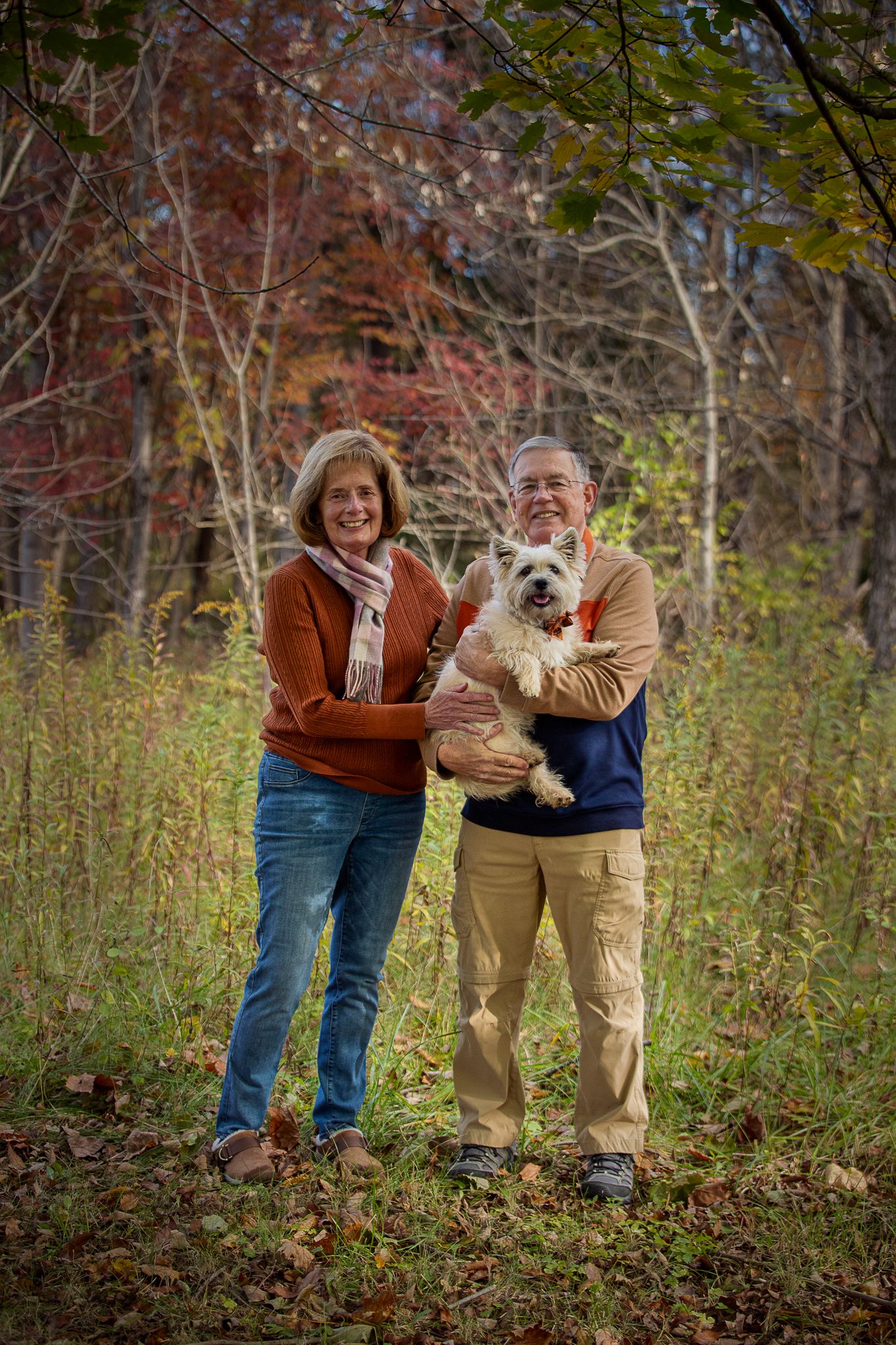Dog parents hold their terrier together in a wooded area