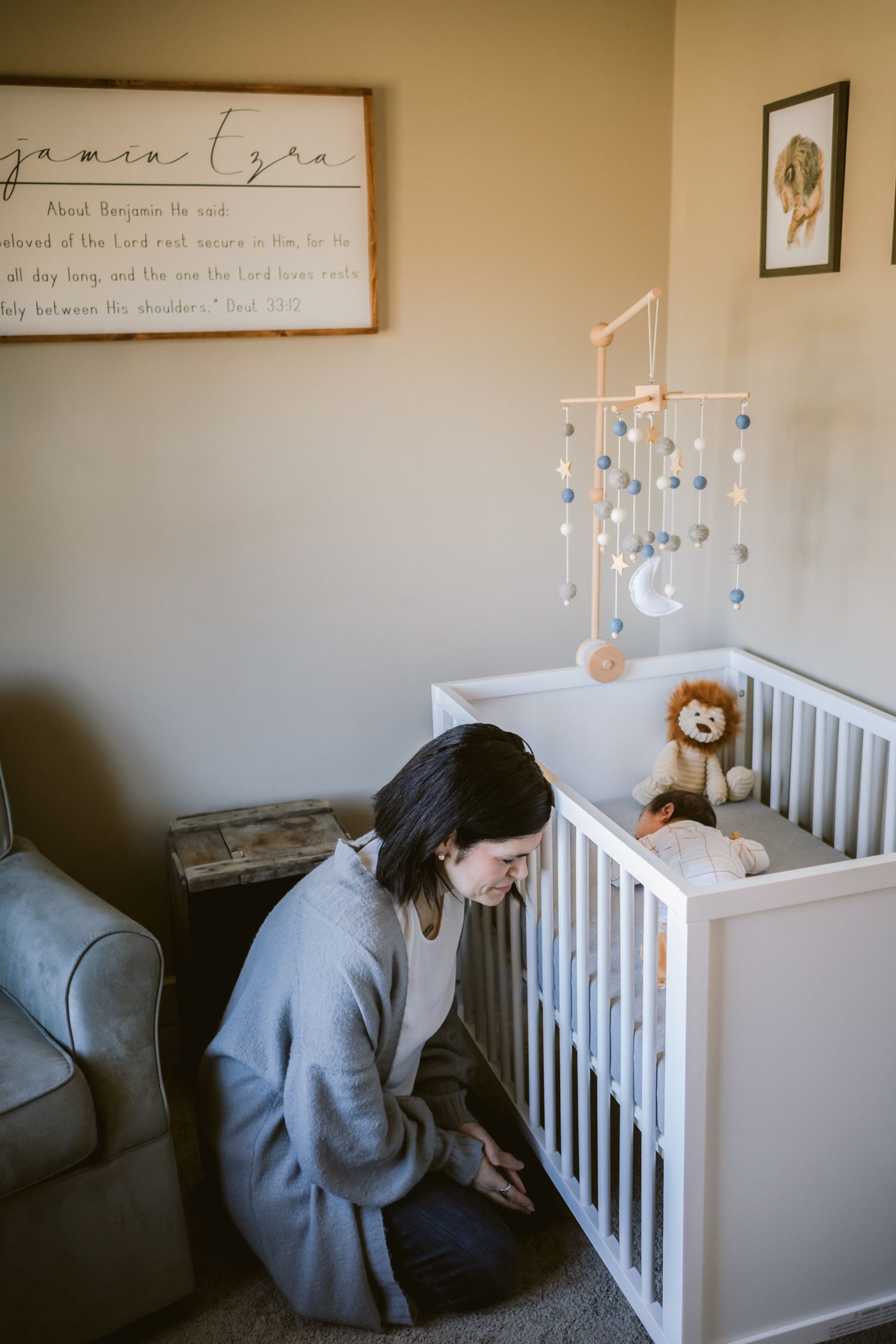 A mother prays next to her sleeping newborn in the baby's nursery during a newborn lifestyle photo shoot in Haverhill, Massachusetts.