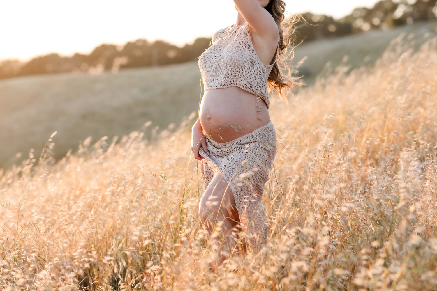 Golden hour maternity photos of expectant mother in tan cropped crochet in golden wheat field. Lakes Region Alton maternity photographer.