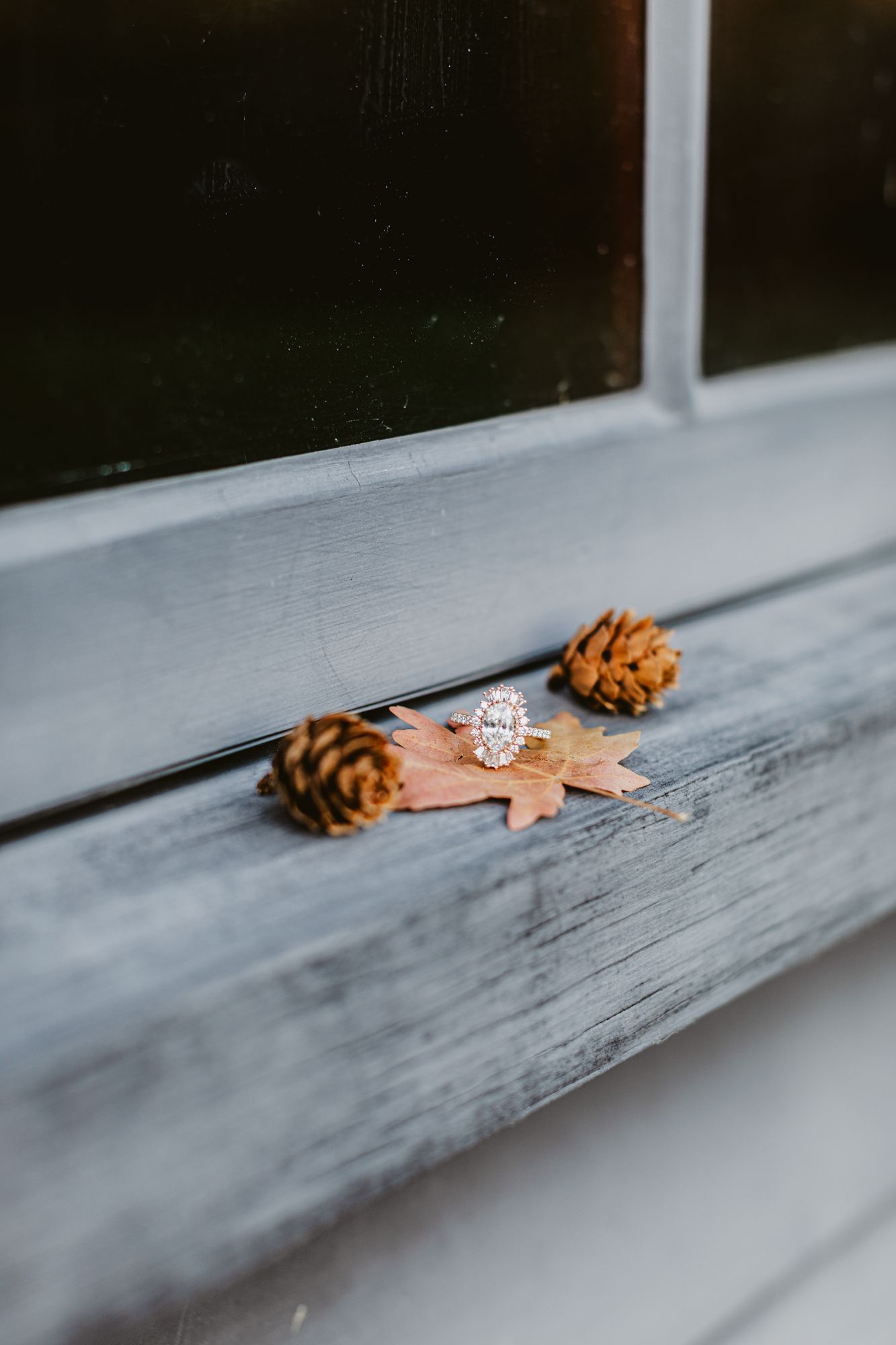 Vintage gold diamond, engagement ring rests on a fall maple leaf with tiny acorns aside it on a weathered blue window ledge in Concord, MA.