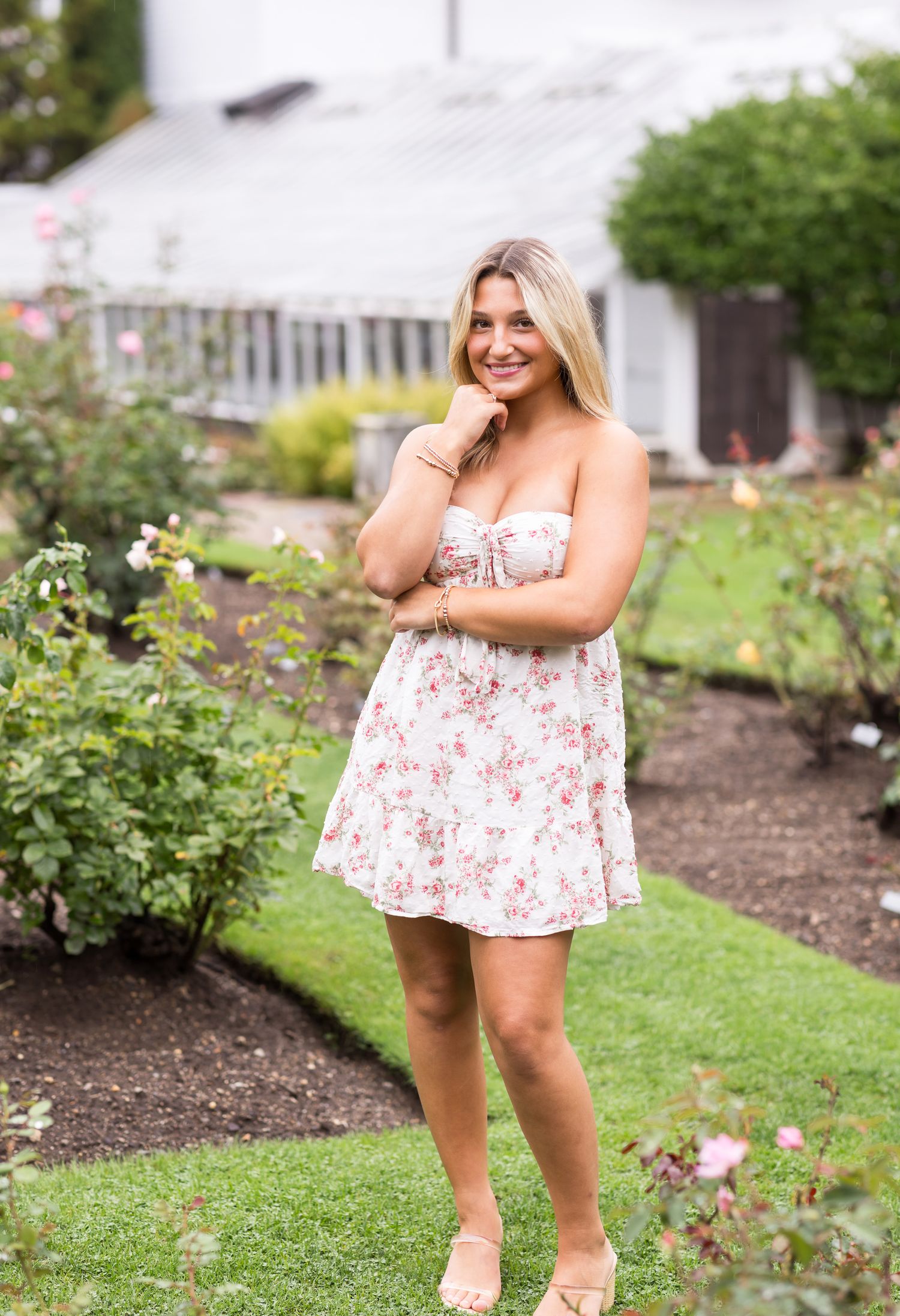 Young lady with blond hair wears a white floral dress at Fuller Gardens in the Seacoast region of Hampton, New Hampshire for senior photos.