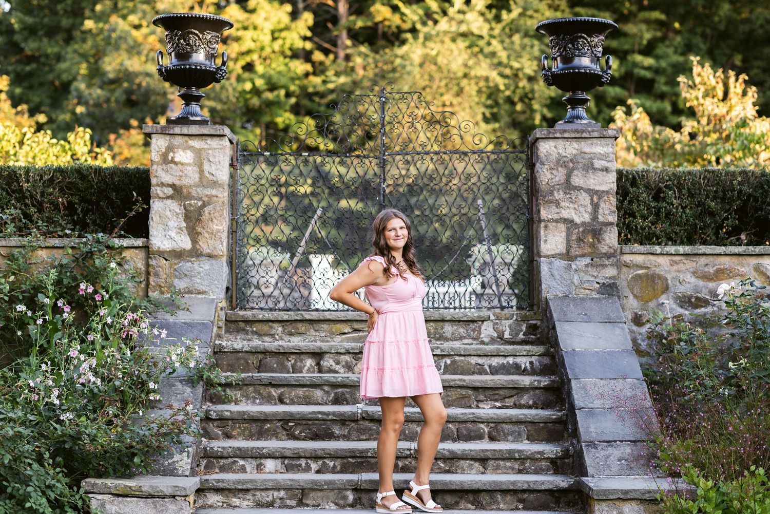 Stevens Coolidge Estate North Andover senior photoshoot of a girl wearing a pink dress posing in front of stone steps in a garden setting.