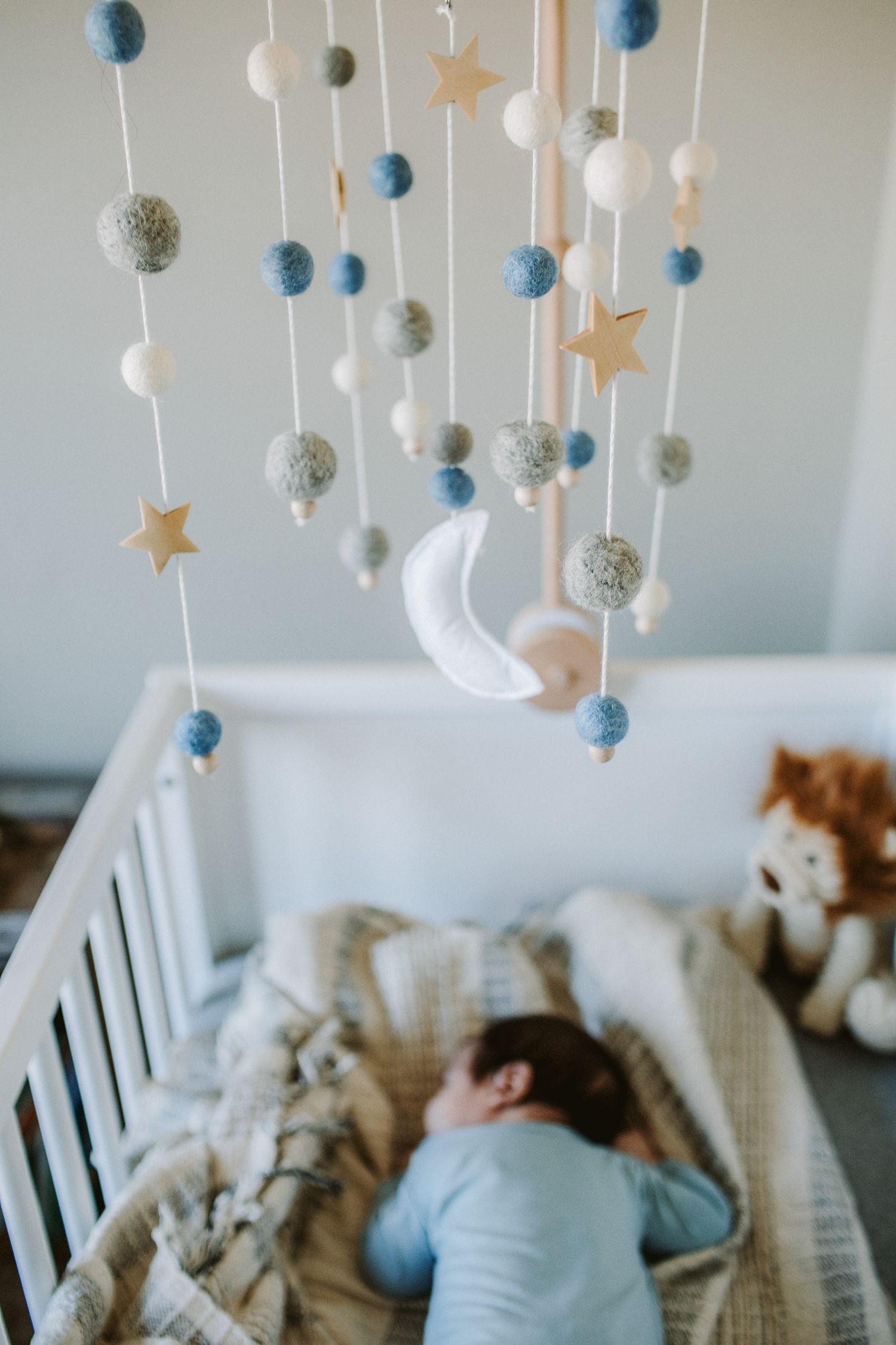 Newborn baby boy sleeps on his belly in his crib with a star and planet mobile hanging over him during a newborn photo session in Haverhill.
