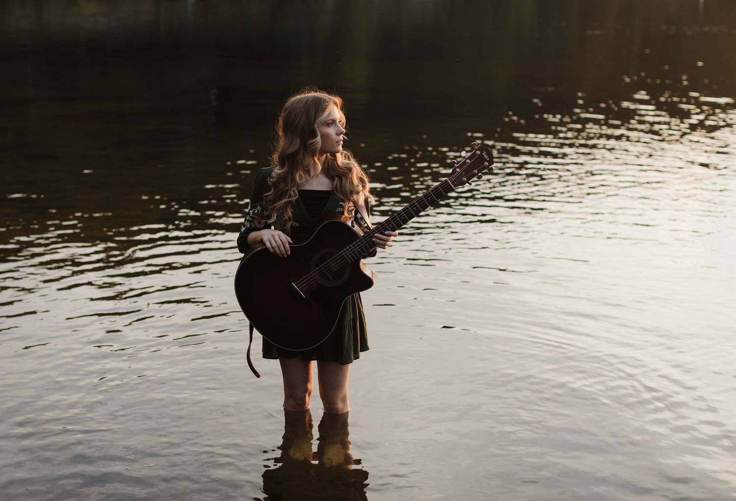 Rachel Delong, Christian musician, poses in a green dress holding her guitar in Lake Sunapee New Hampshire at golden hour for portraits.