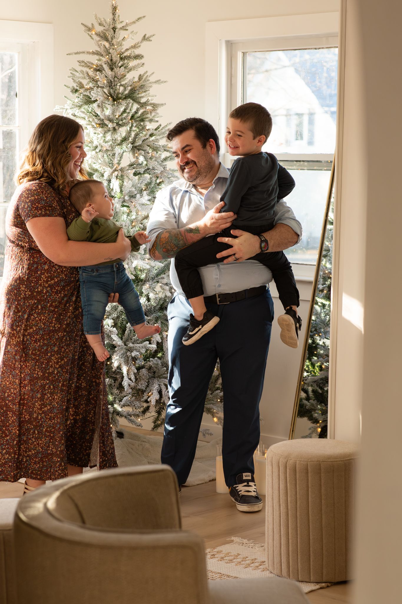 Happy family with two young boys laughing together in a festive living room with a flocked Christmas tree.