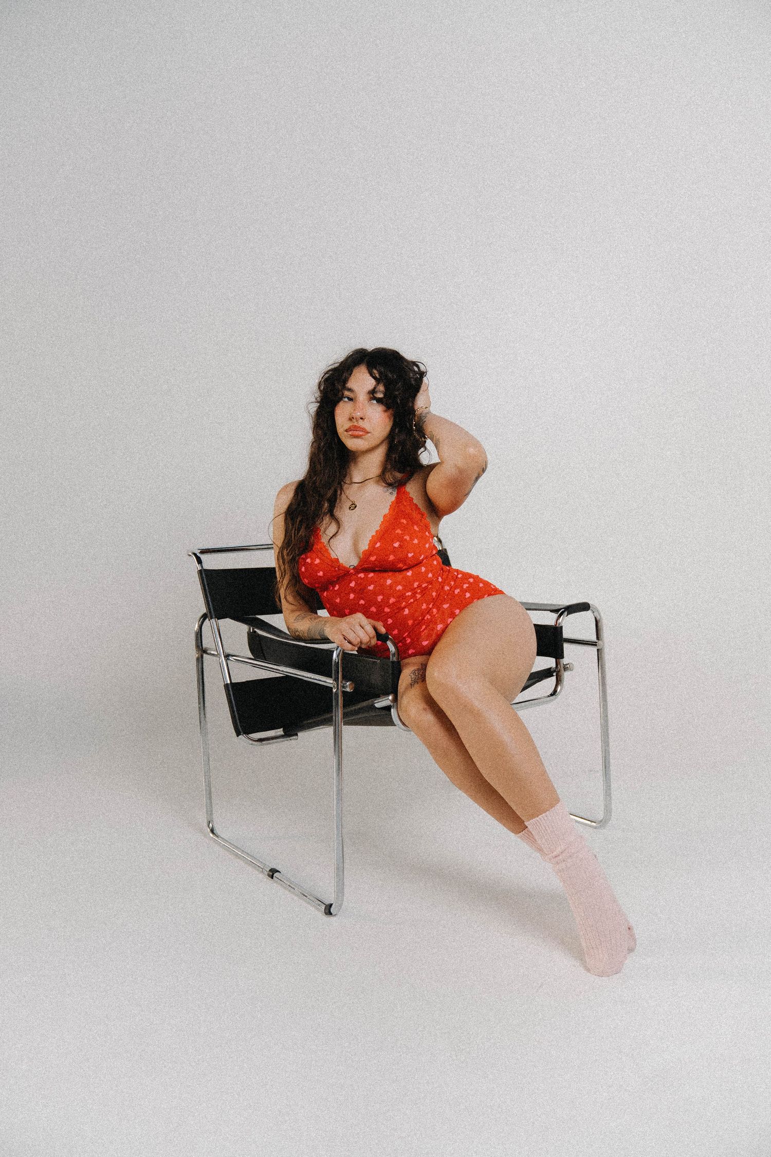Woman in red polka dot mini dress sitting in modern chair with pink socks on white background.